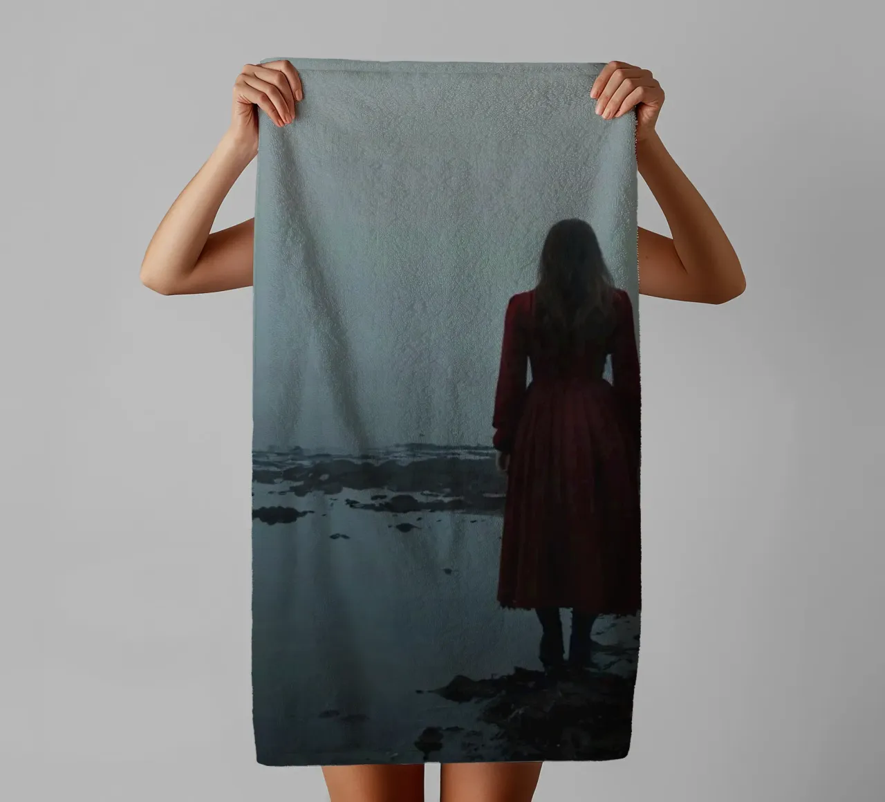 Une femme vêtue d'une robe rouge se tient debout, contemplative, au bord d'une rivière brumeuse. serviette de bain de DesignDoodle