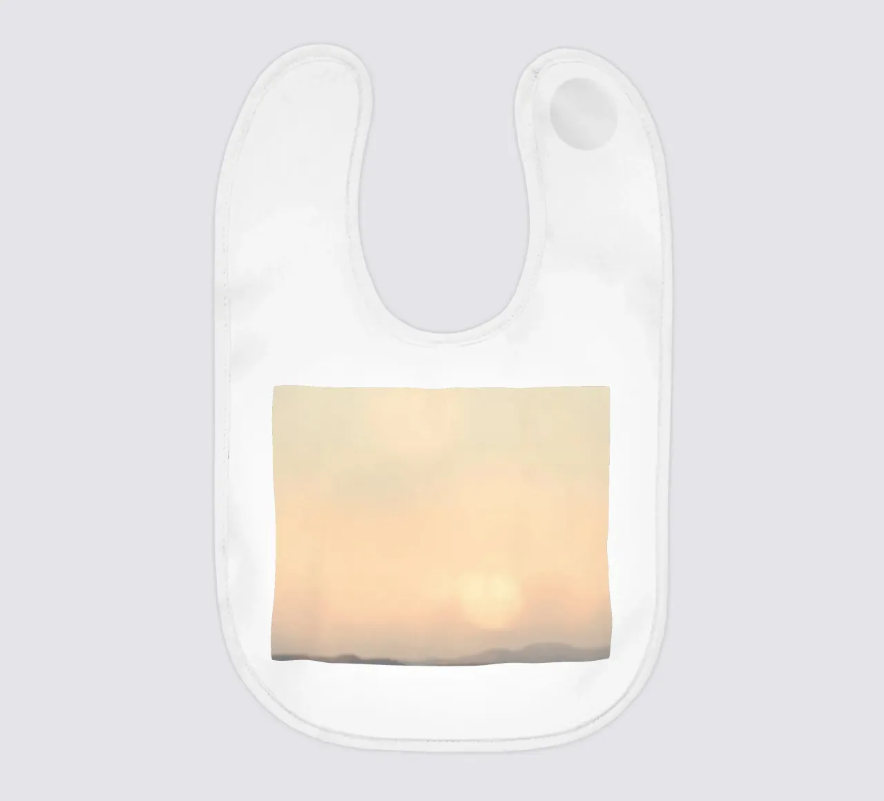 Sunset casting a warm glow over distant mountains and cloude baby bib by DesignDoodle