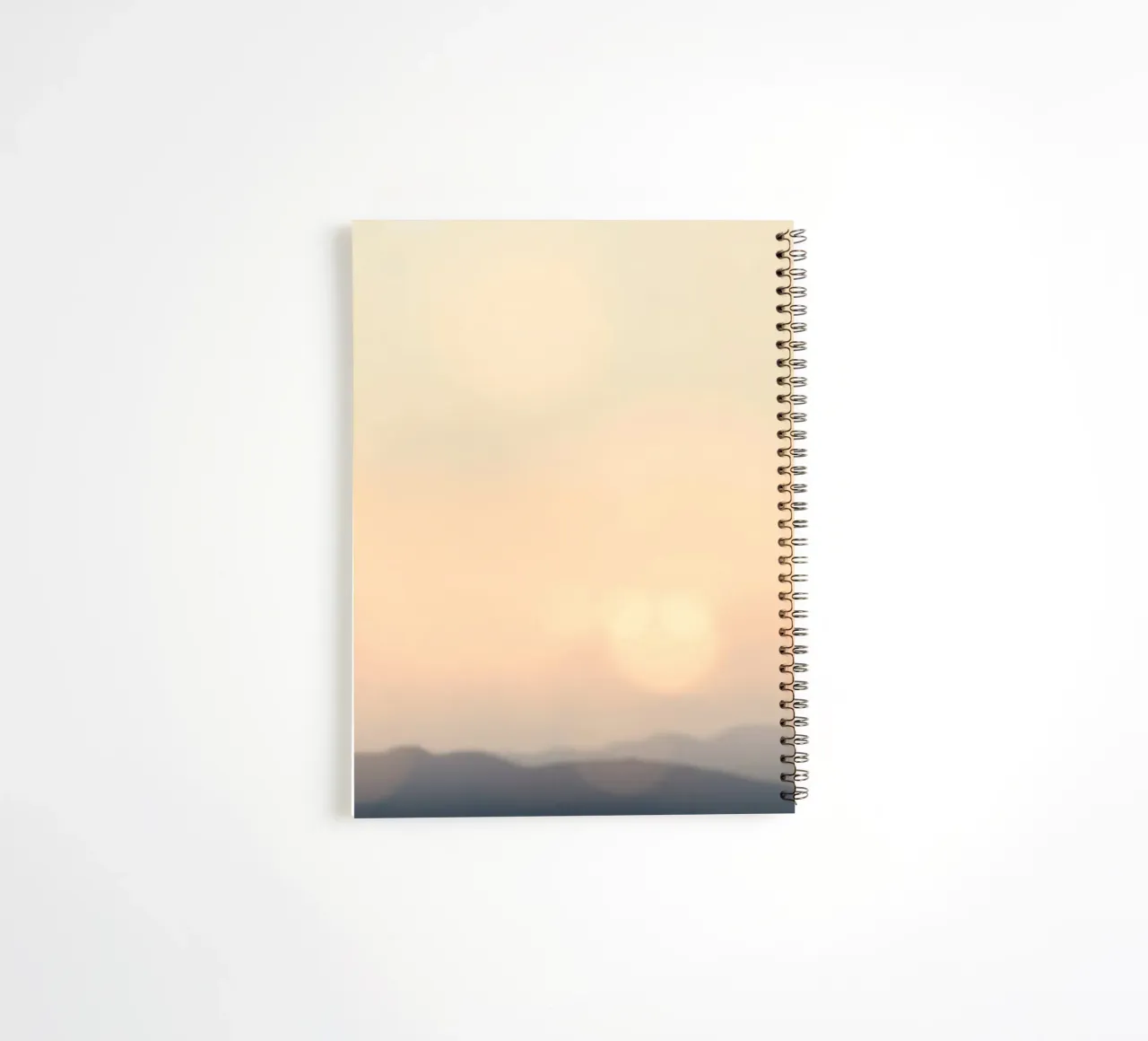 Sunset casting a warm glow over distant mountains and cloude spiral notebook by DesignDoodle