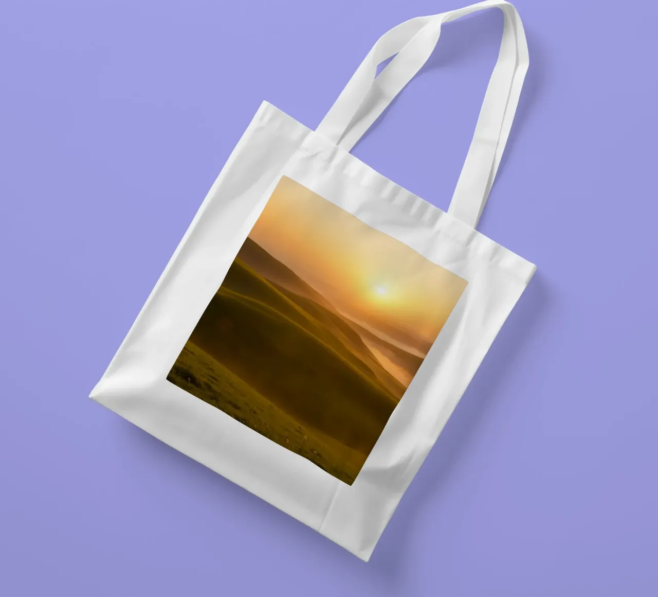 Sunset over rolling green hills with mist creating a serene tote bag by DesignDoodle