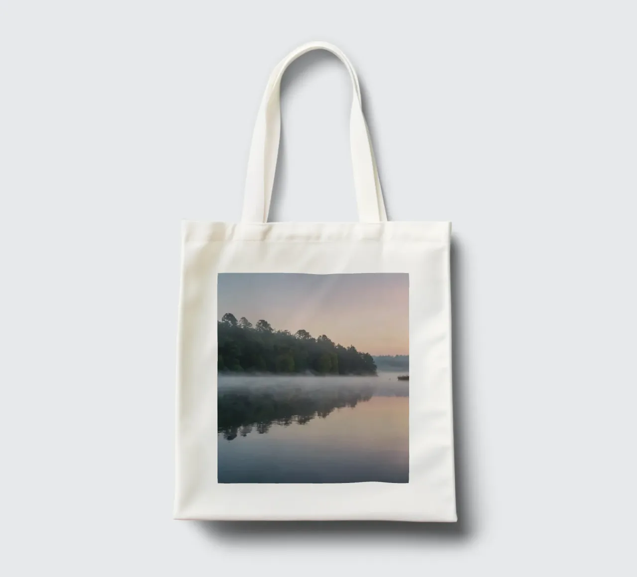 mist rises over a tranquil lake surrounded by lush trees tote bag by DesignDoodle