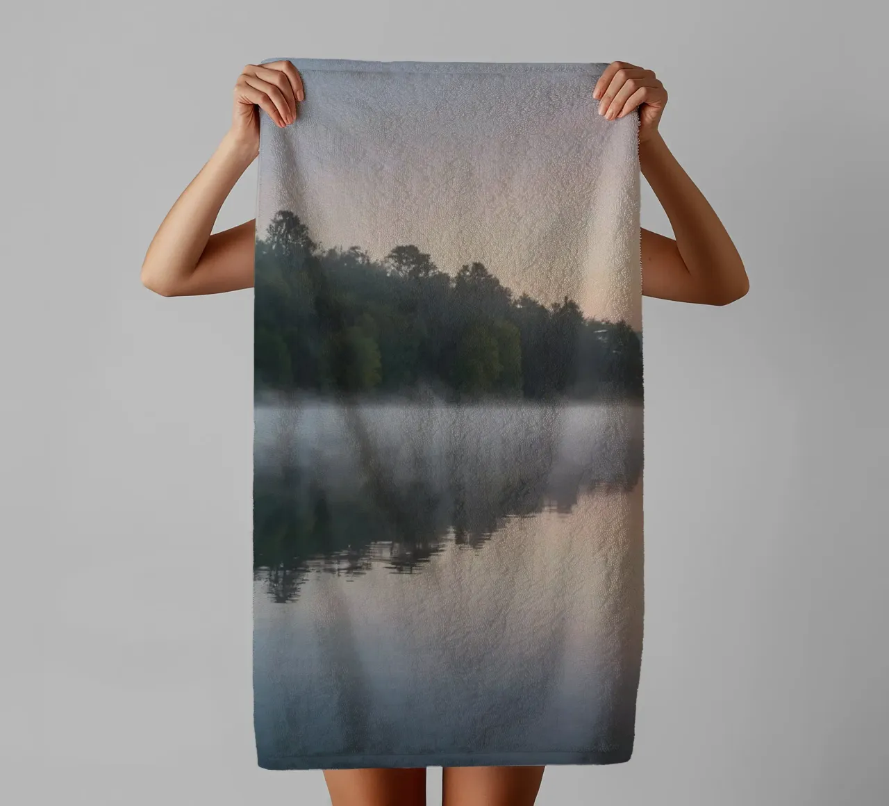 mist rises over a tranquil lake surrounded by lush trees towel by DesignDoodle