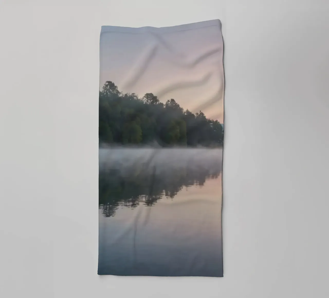 mist rises over a tranquil lake surrounded by lush trees towel by DesignDoodle