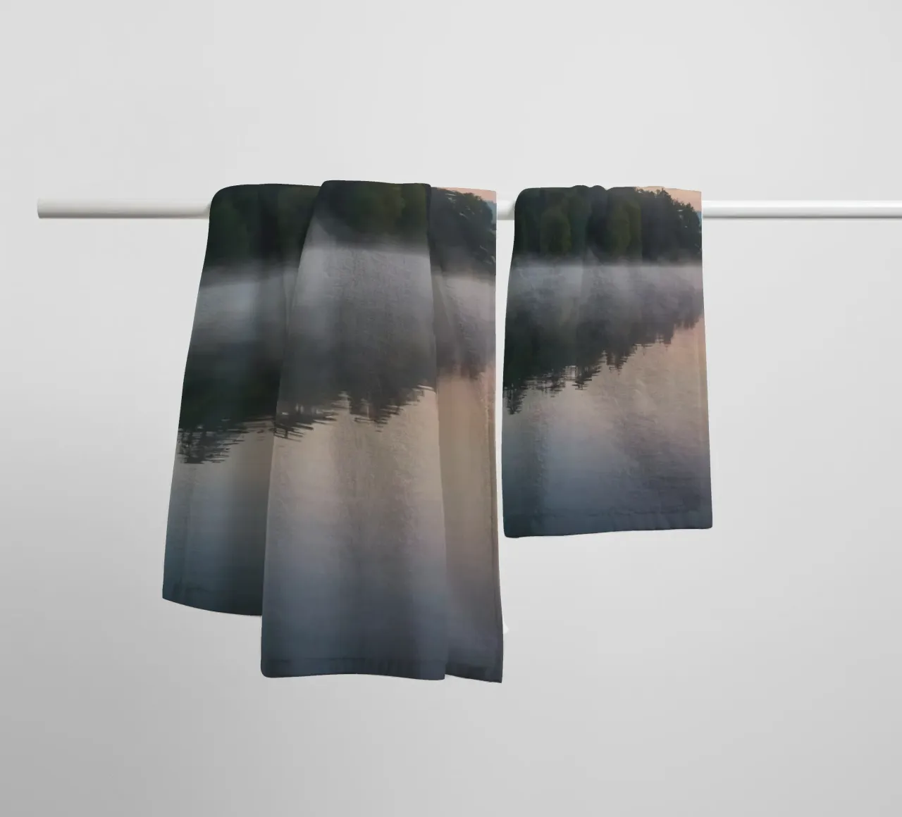 mist rises over a tranquil lake surrounded by lush trees towel by DesignDoodle