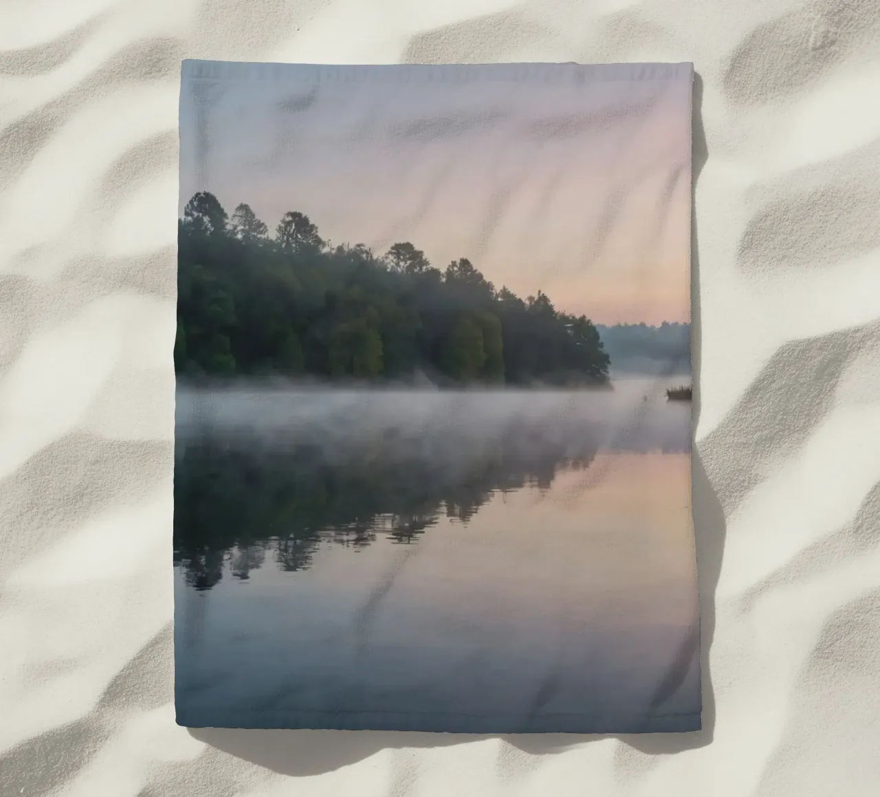 mist rises over a tranquil lake surrounded by lush trees beach towel by DesignDoodle