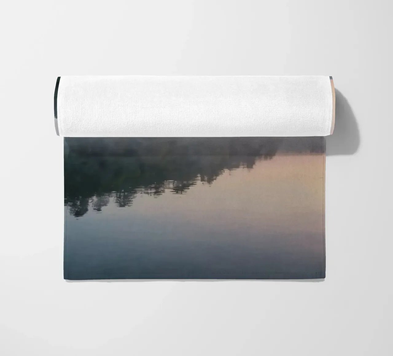 mist rises over a tranquil lake surrounded by lush trees beach towel by DesignDoodle