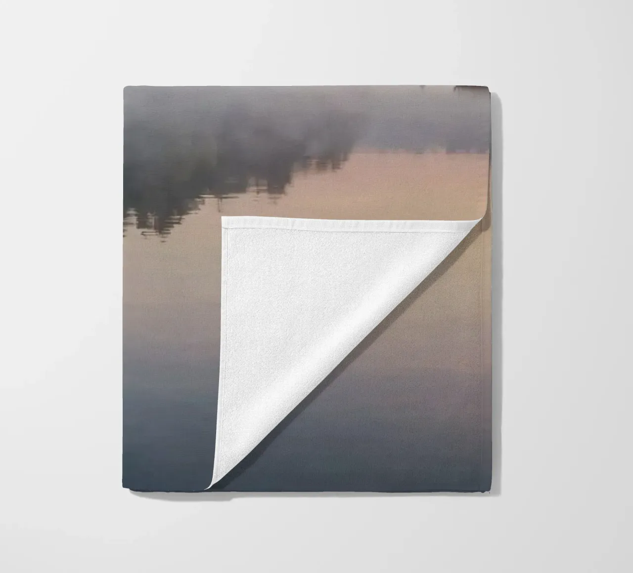 mist rises over a tranquil lake surrounded by lush trees beach towel by DesignDoodle