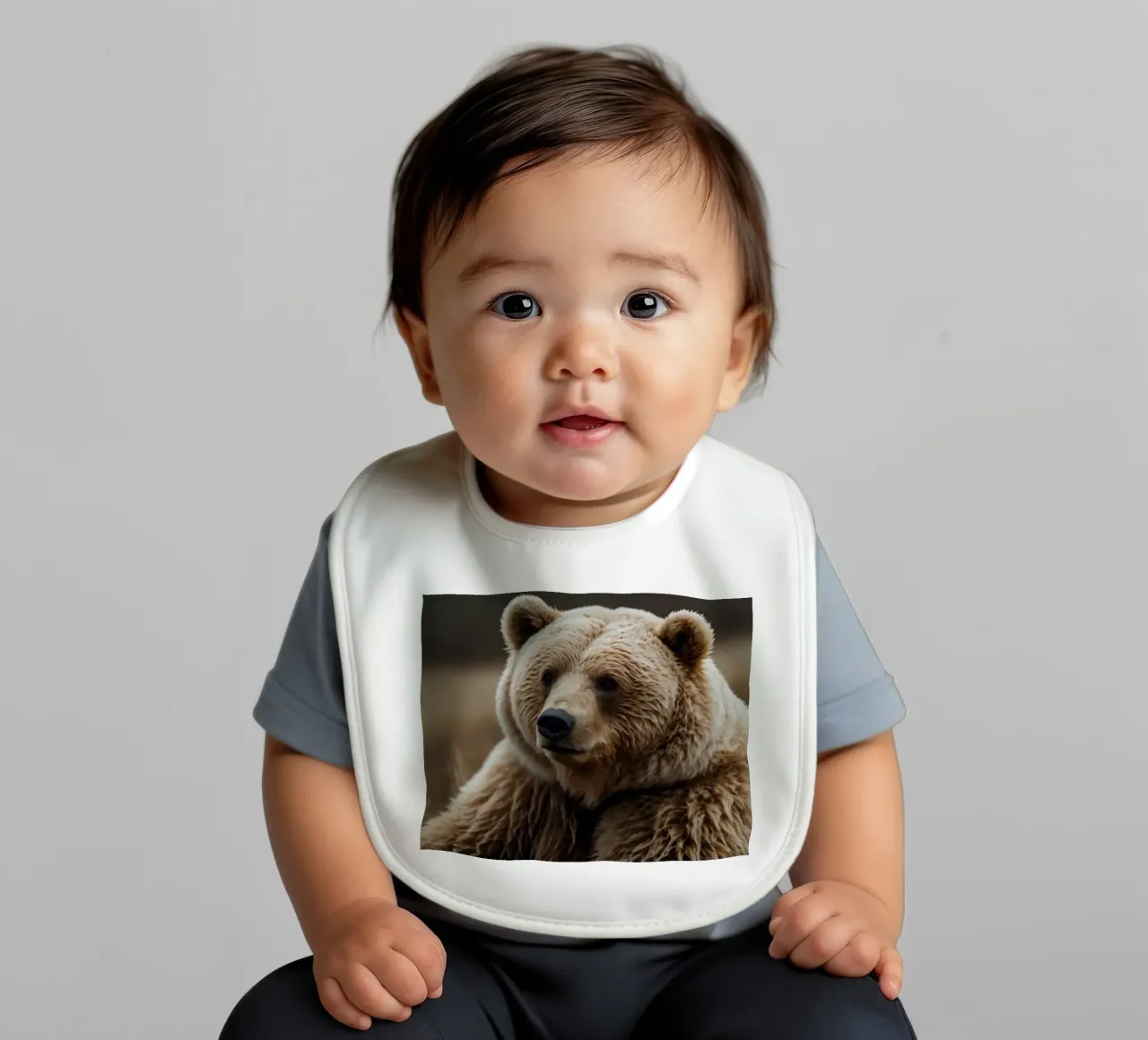 A close-up view of a brown bear resting in a grassy field baby bib by DesignDoodle