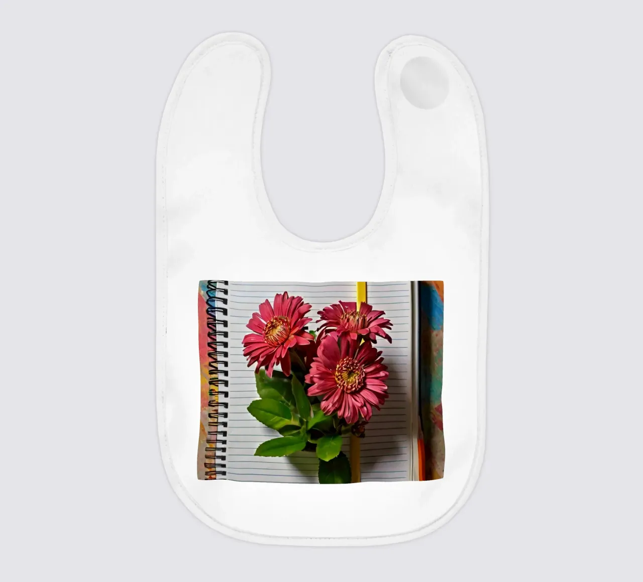 Ein leuchtendes Notizbuch mit rosafarbenen Blumen auf dem Kopf, die Babylätzchen von DesignDoodle