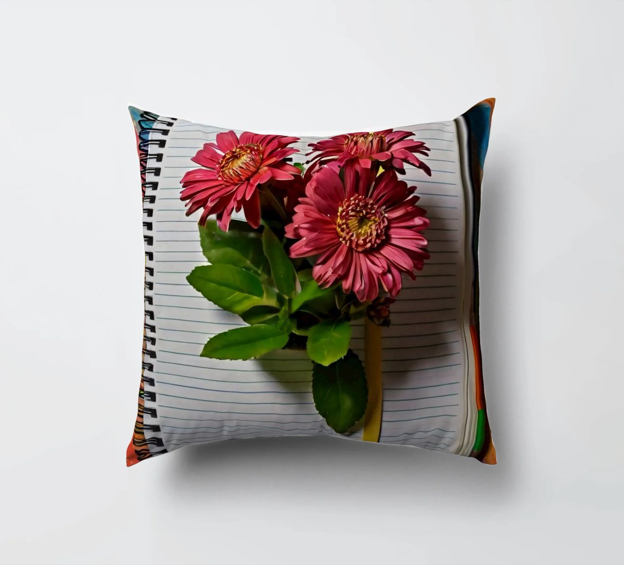 Un taccuino vivace con fiori rosa appoggiati in cima, che mette in mostra cuscino da DesignDoodle