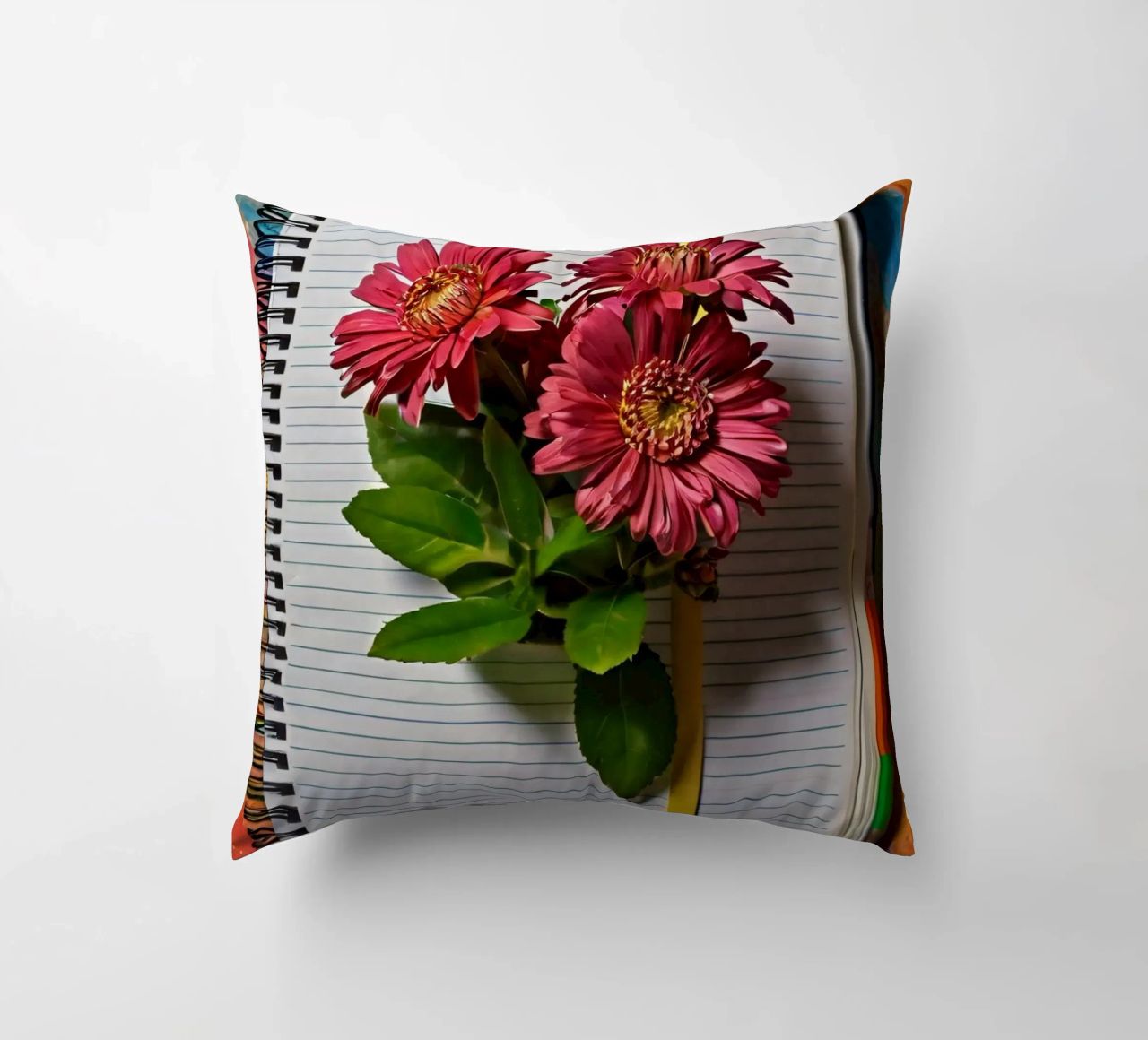 Un taccuino vivace con fiori rosa appoggiati in cima, che mette in mostra cuscino da DesignDoodle