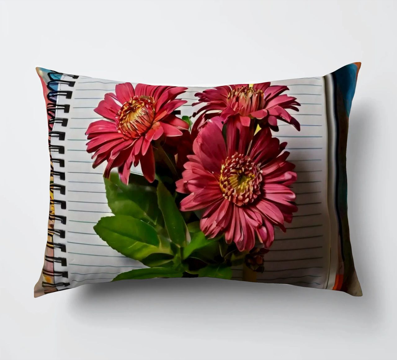 Un taccuino vivace con fiori rosa appoggiati in cima, che mette in mostra cuscino da DesignDoodle