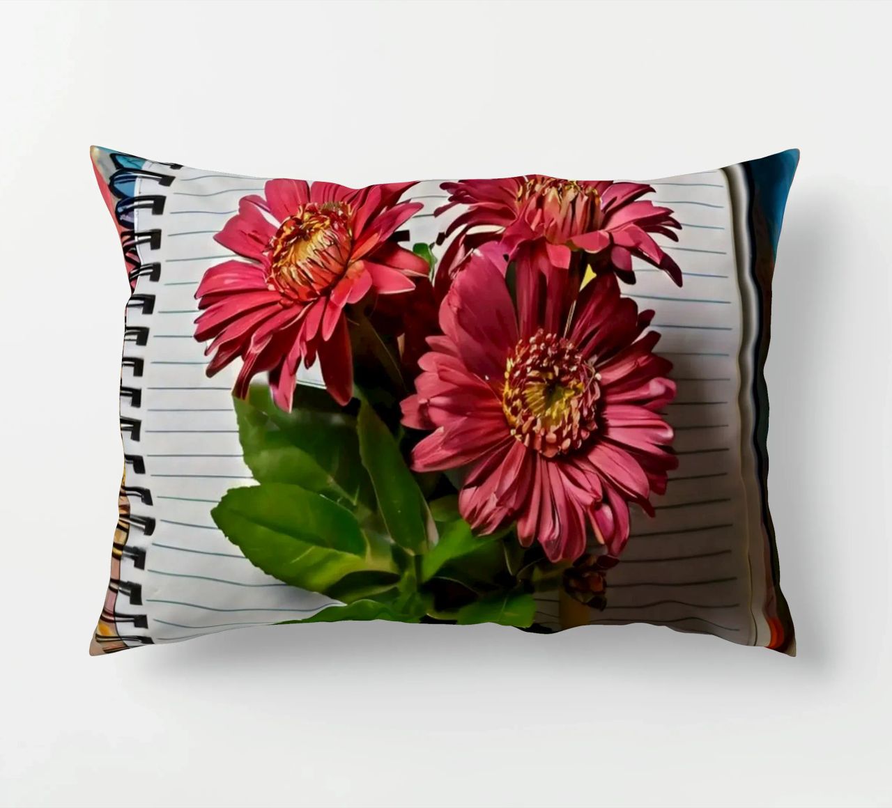 Un taccuino vivace con fiori rosa appoggiati in cima, che mette in mostra cuscino da DesignDoodle