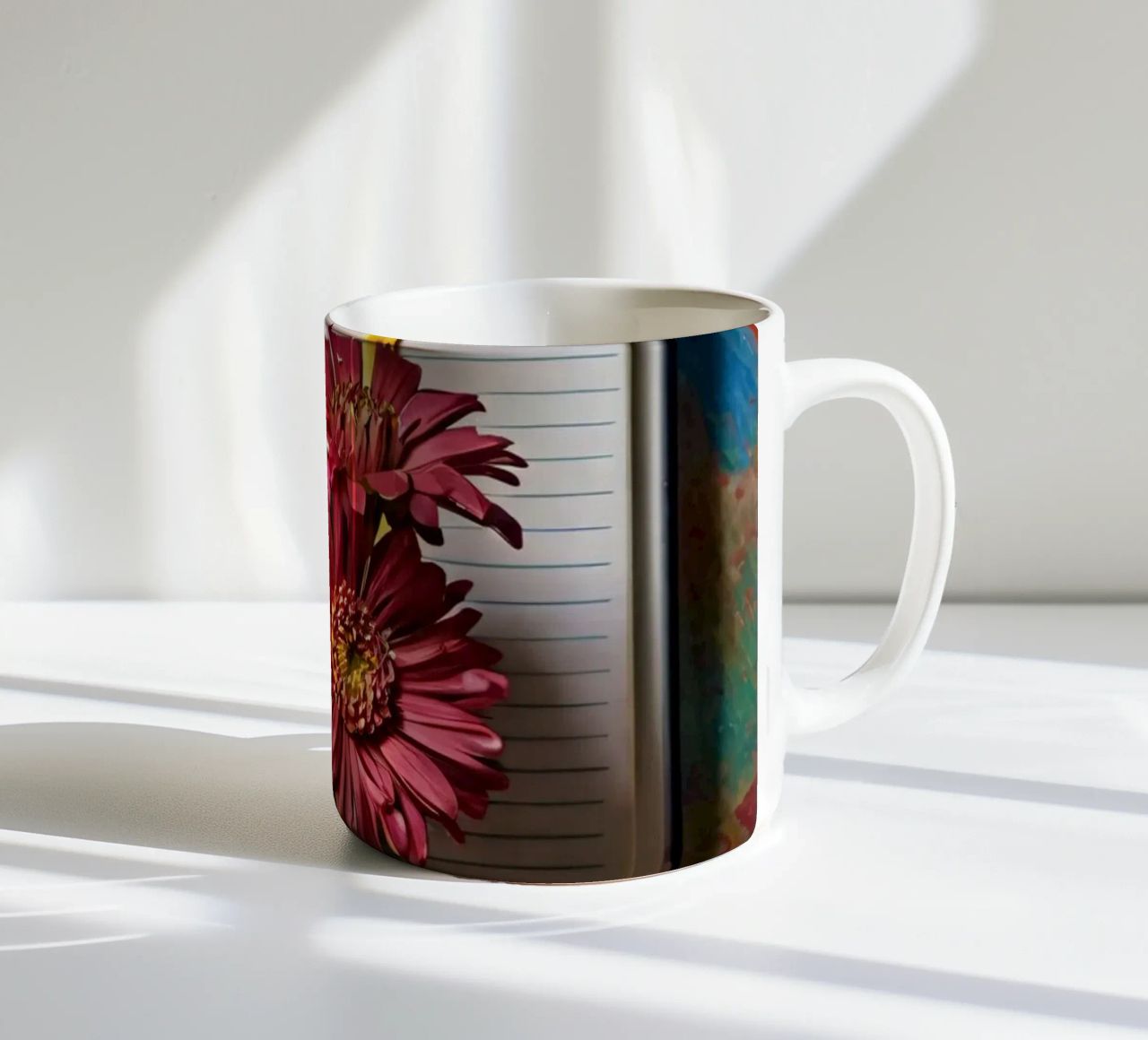 Un taccuino vivace con fiori rosa appoggiati in cima, che mette in mostra tazza in ceramica da DesignDoodle