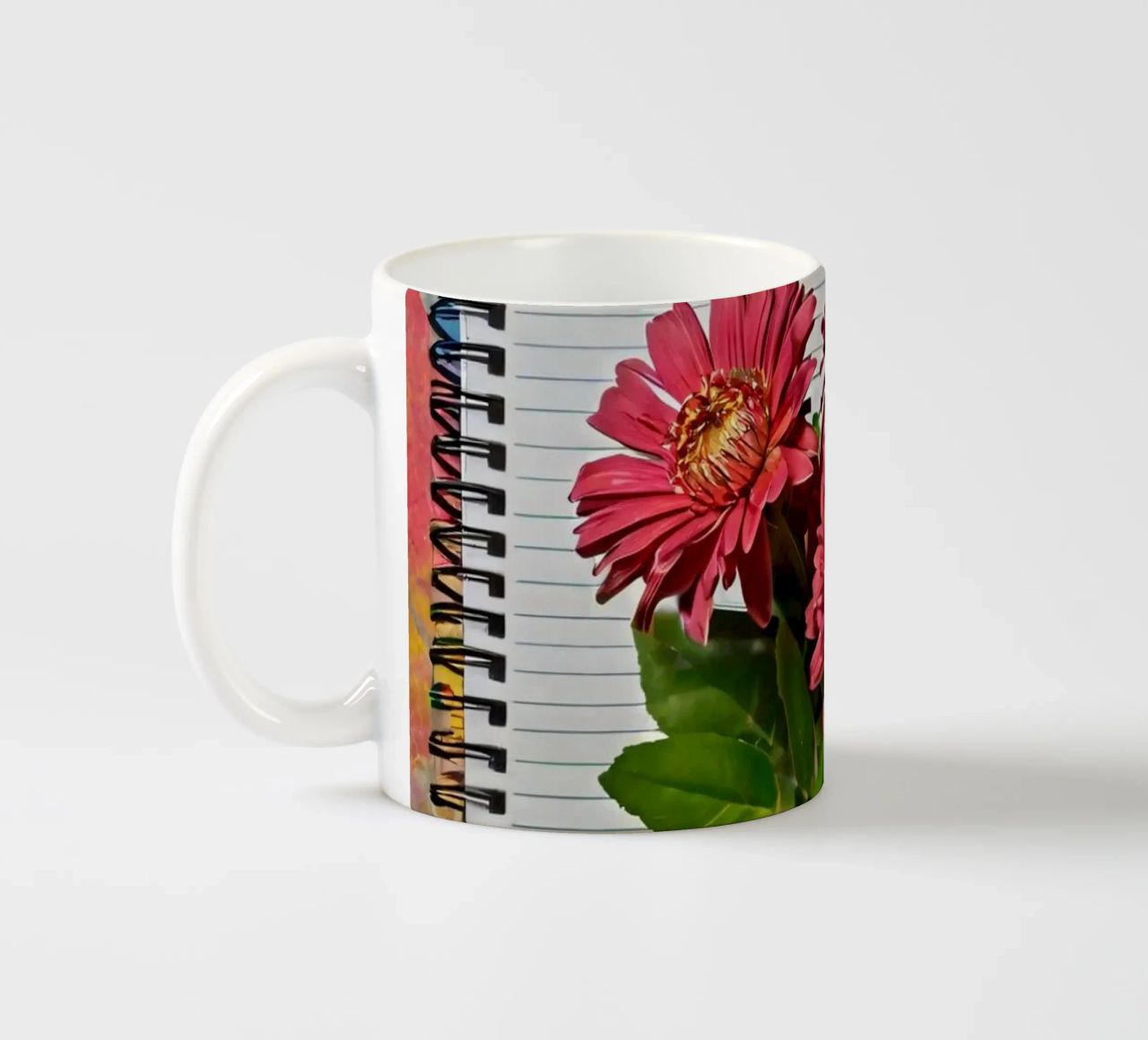 Un taccuino vivace con fiori rosa appoggiati in cima, che mette in mostra tazza in ceramica da DesignDoodle
