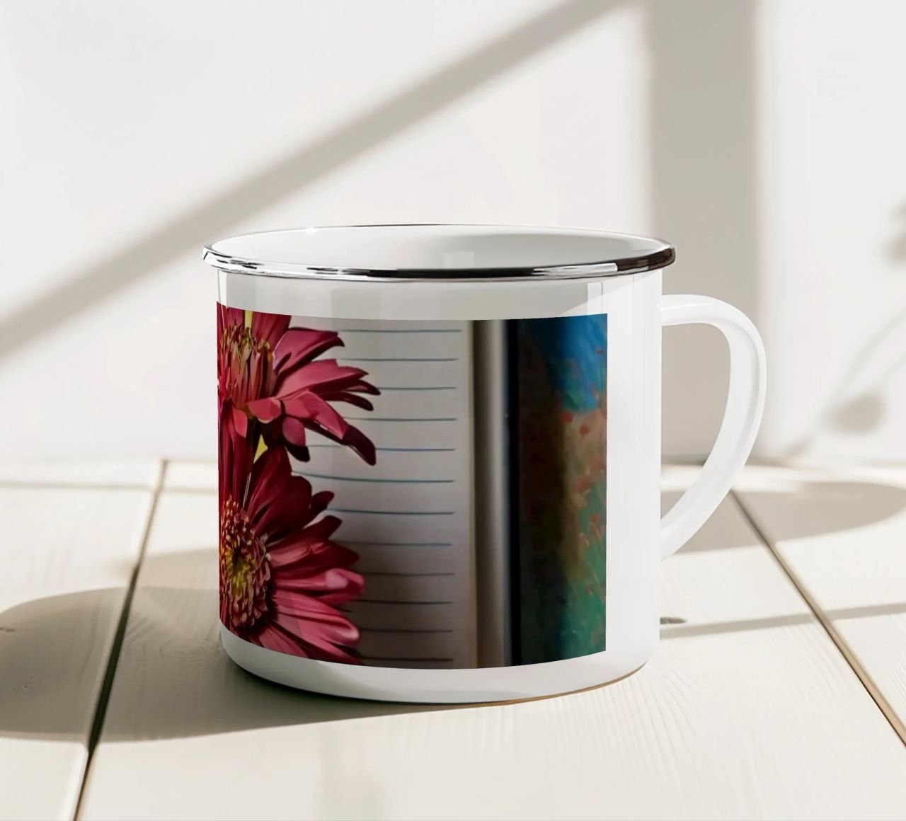 Un taccuino vivace con fiori rosa appoggiati in cima, che mette in mostra tazza in smalto da DesignDoodle