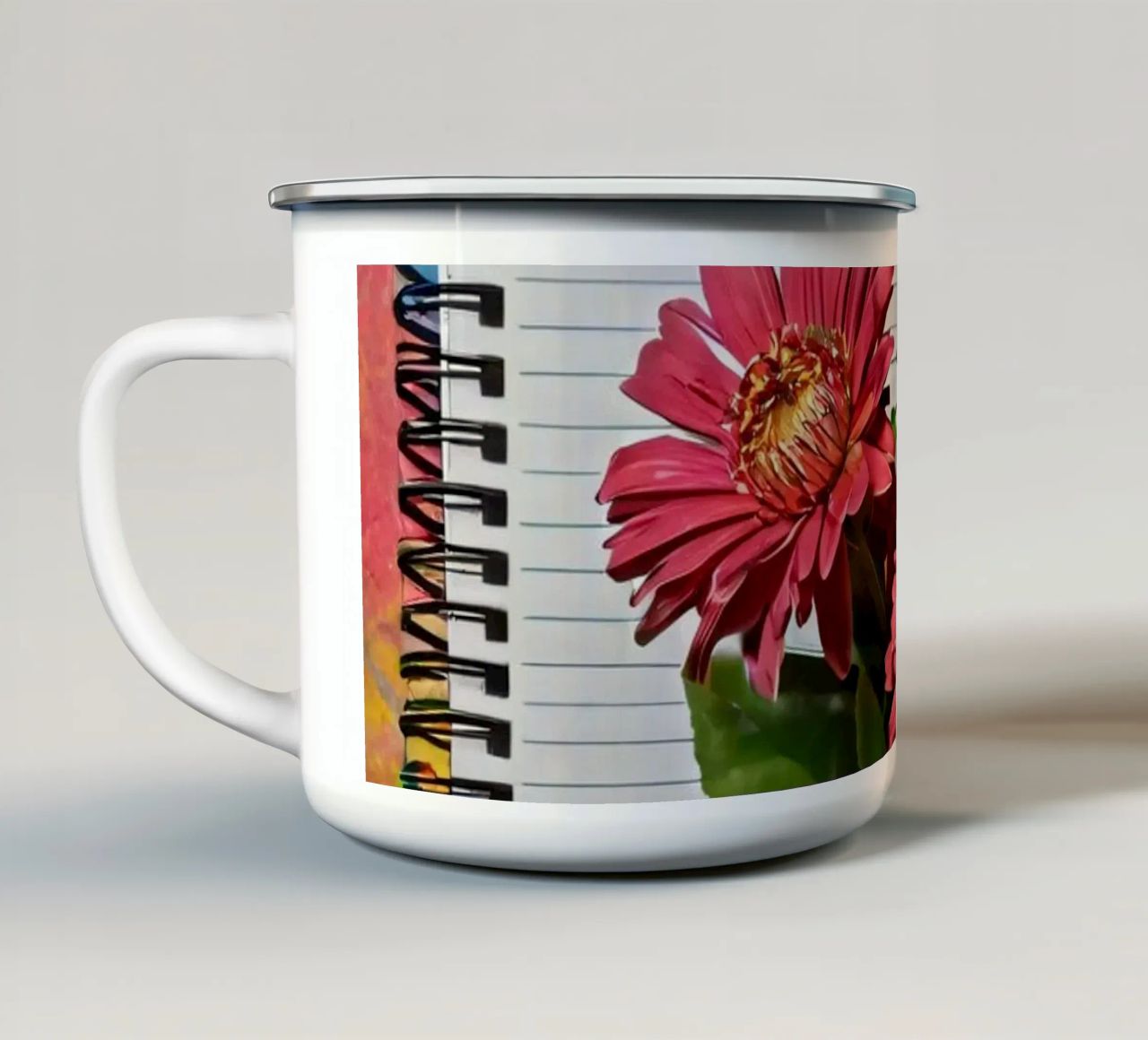 Un taccuino vivace con fiori rosa appoggiati in cima, che mette in mostra tazza in smalto da DesignDoodle