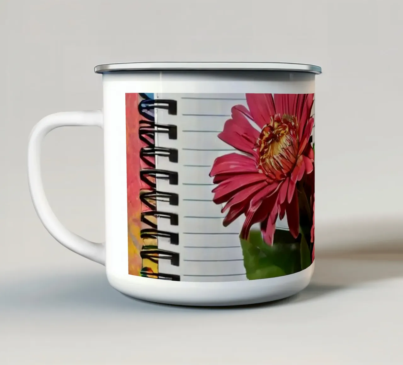 Un taccuino vivace con fiori rosa appoggiati in cima, che mette in mostra tazza in smalto da DesignDoodle