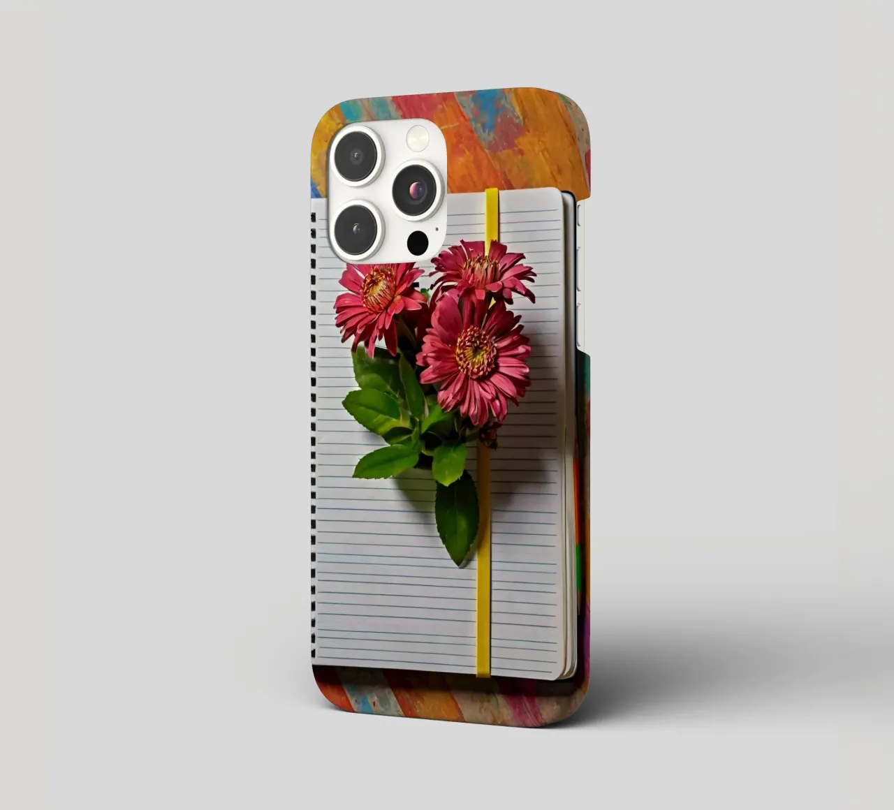 Un taccuino vivace con fiori rosa appoggiati in cima, che mette in mostra cover iphone da DesignDoodle