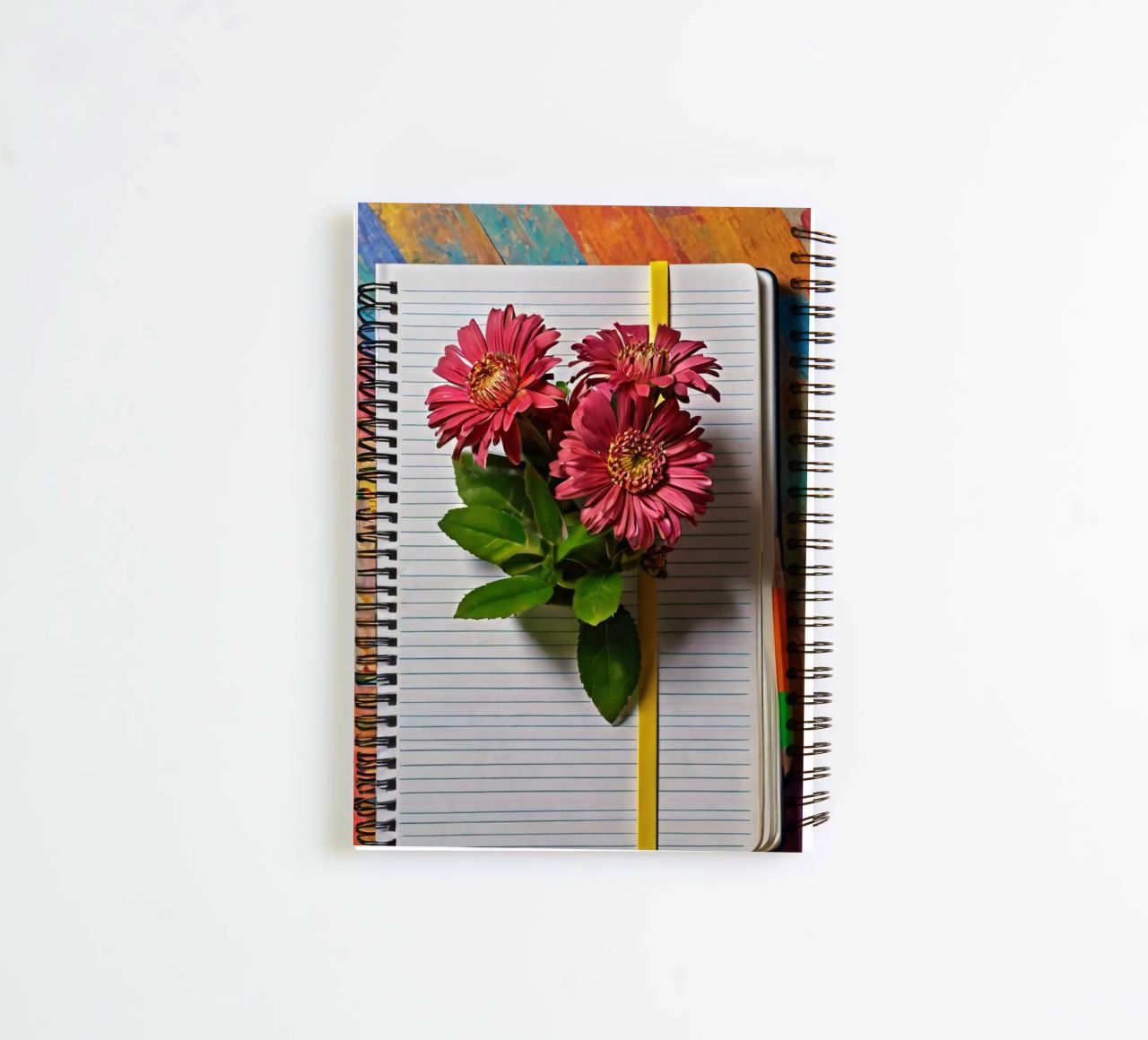 Un taccuino vivace con fiori rosa appoggiati in cima, che mette in mostra diario ad anelli da DesignDoodle