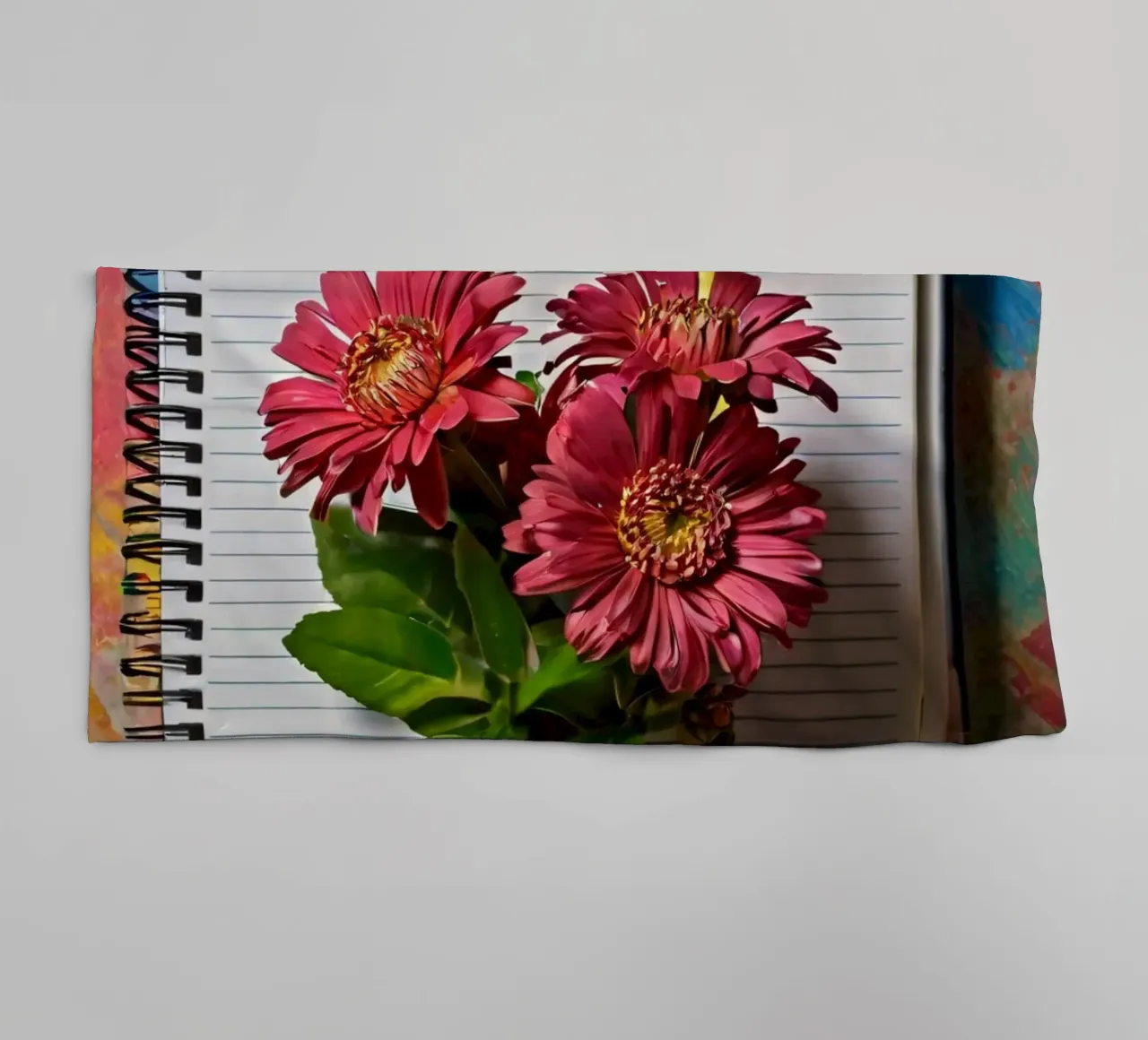 Un taccuino vivace con fiori rosa appoggiati in cima, che mette in mostra asciugamano da bagno da DesignDoodle