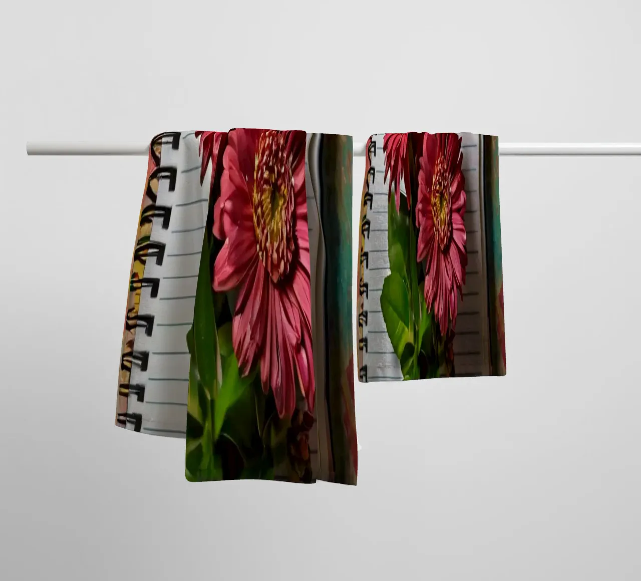 Un taccuino vivace con fiori rosa appoggiati in cima, che mette in mostra asciugamano da bagno da DesignDoodle