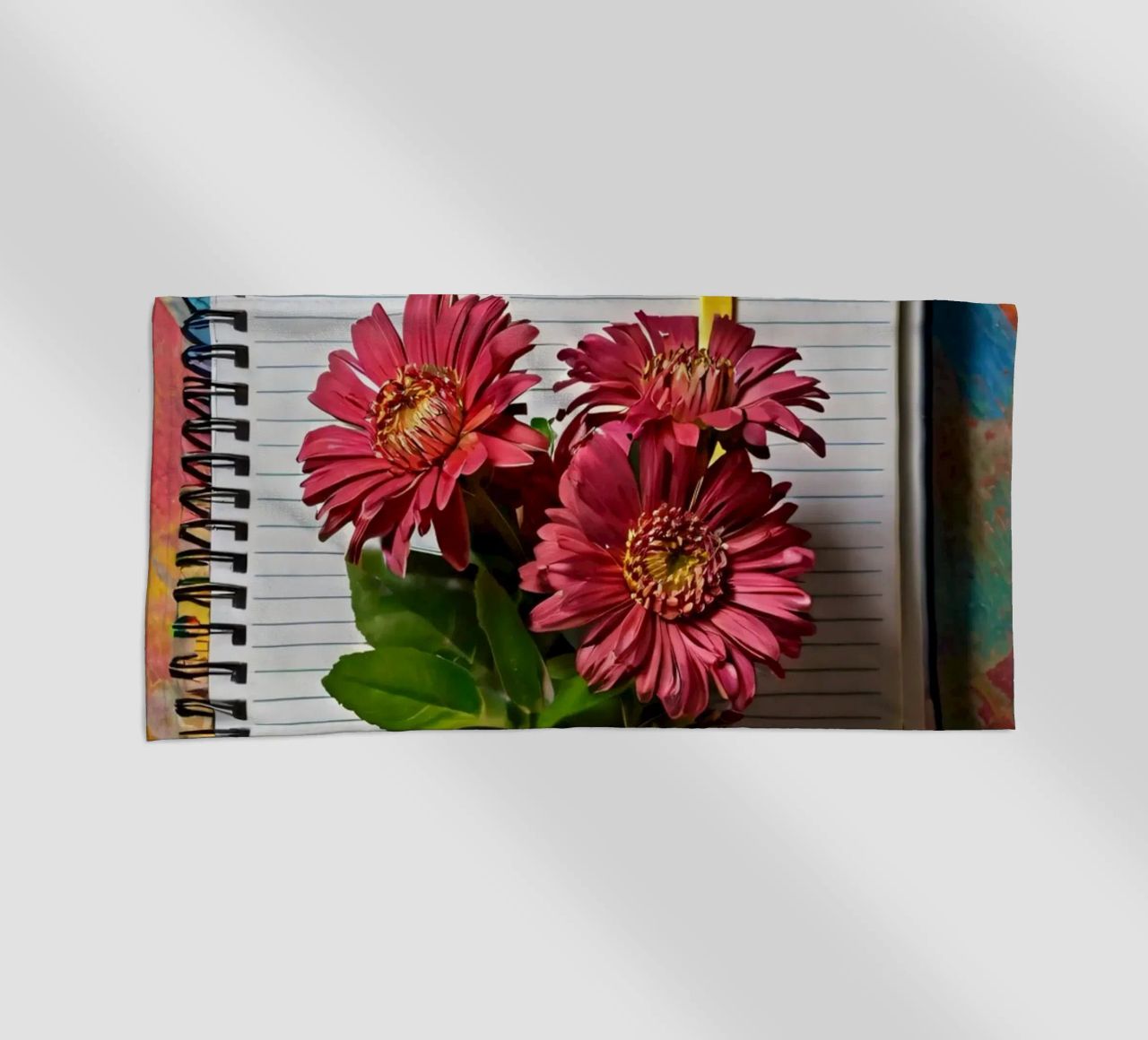 Un taccuino vivace con fiori rosa appoggiati in cima, che mette in mostra telo mare da DesignDoodle