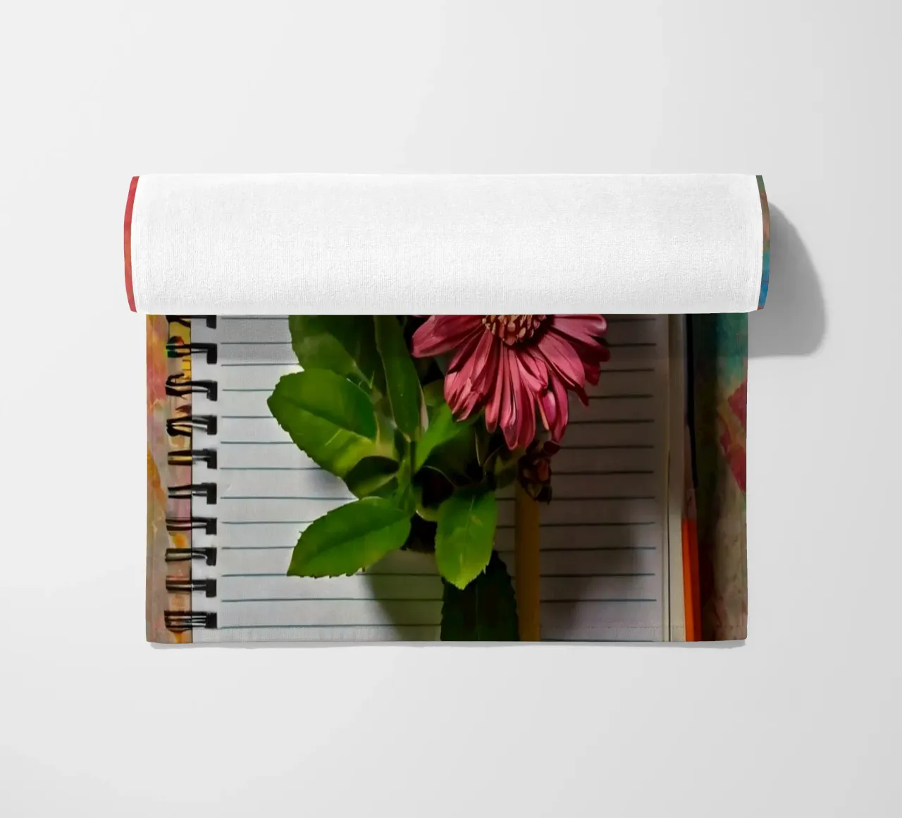 Un taccuino vivace con fiori rosa appoggiati in cima, che mette in mostra telo mare da DesignDoodle
