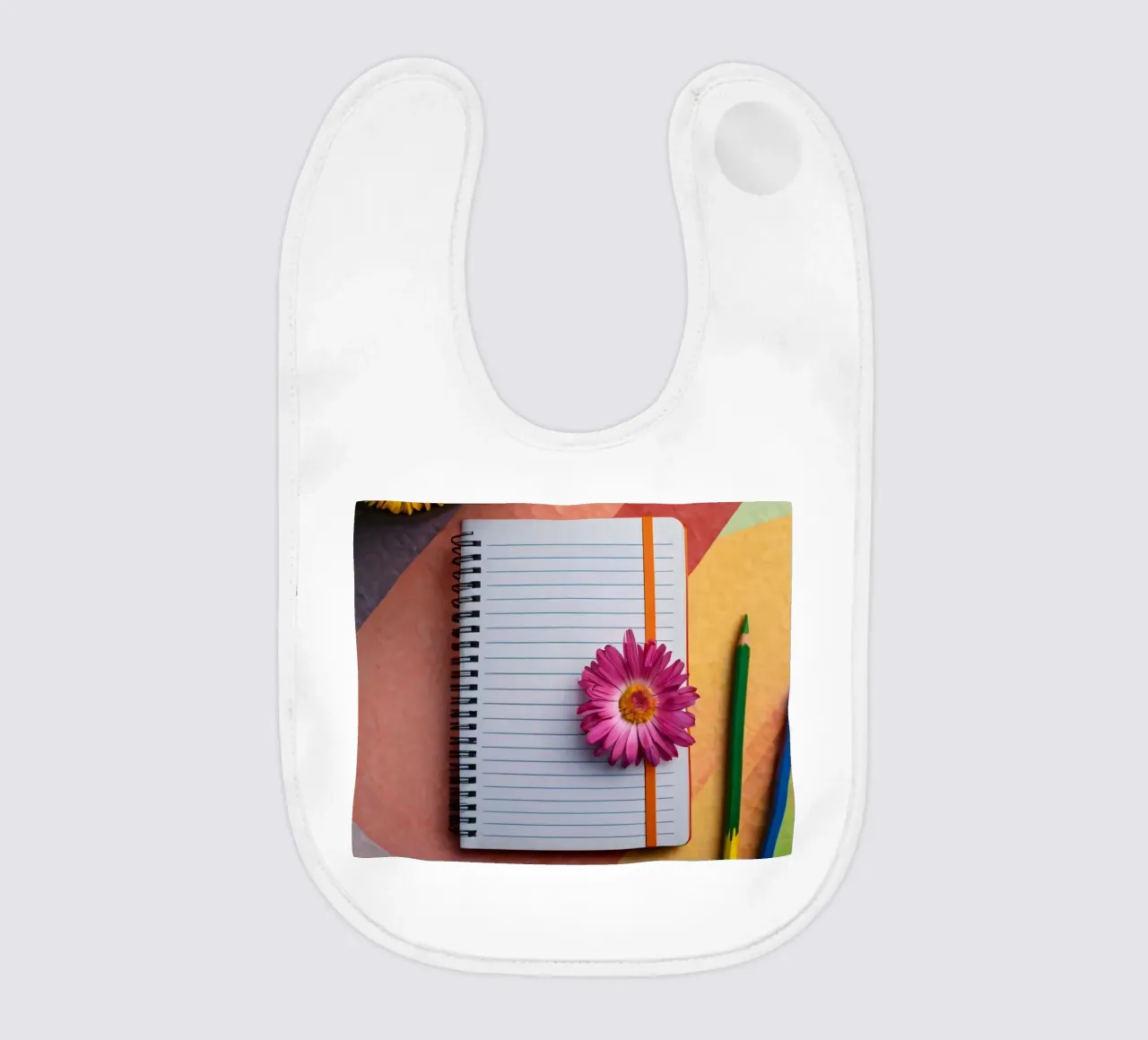 Colorful workspace featuring a notebook with a flower baby bib by DesignDoodle