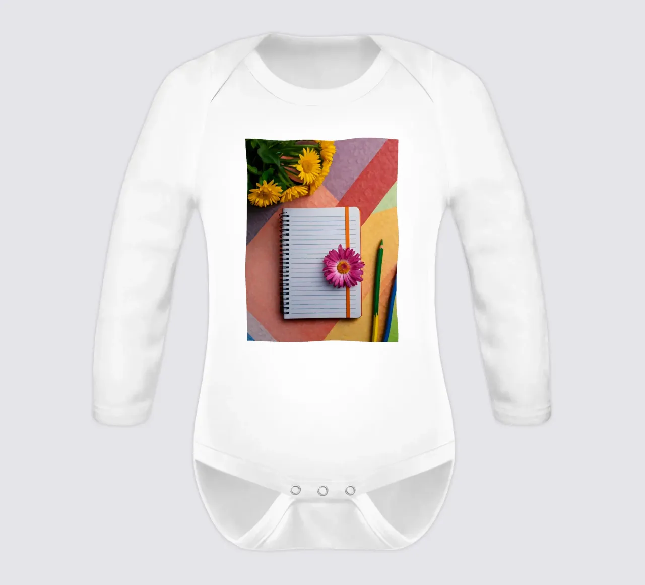 Uno spazio di lavoro colorato con un taccuino con un fiore body neonato maniche lunghe da DesignDoodle
