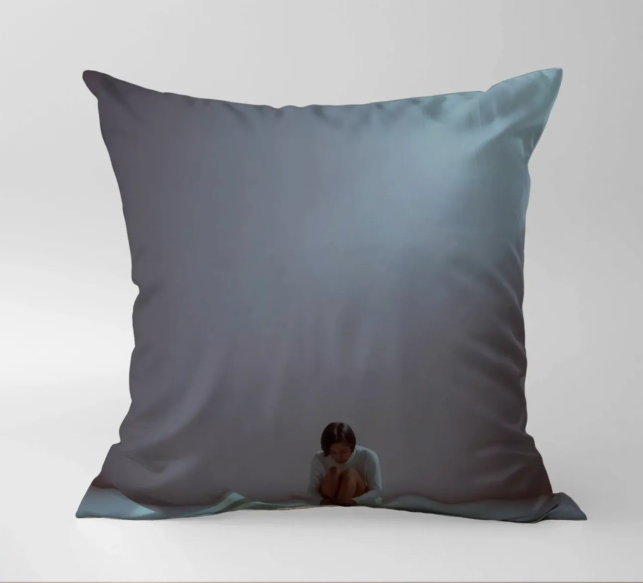 Young woman sits thoughtfully in dimly lit space, reflecting decorative cushion by DesignDoodle