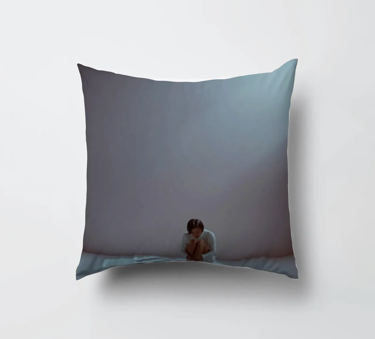 Young woman sits thoughtfully in dimly lit space, reflecting decorative cushion by DesignDoodle