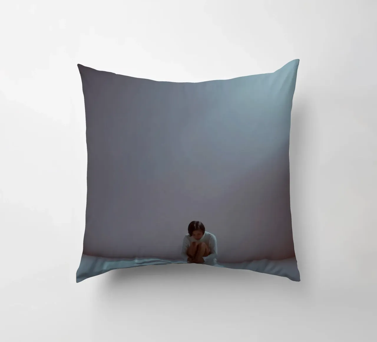 Young woman sits thoughtfully in dimly lit space, reflecting decorative cushion by DesignDoodle