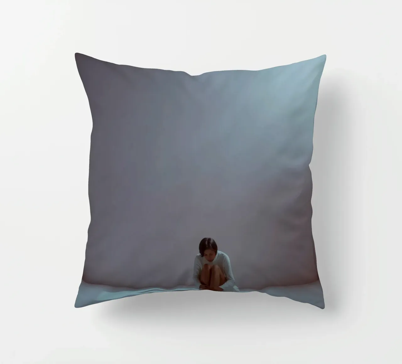 Young woman sits thoughtfully in dimly lit space, reflecting decorative cushion by DesignDoodle