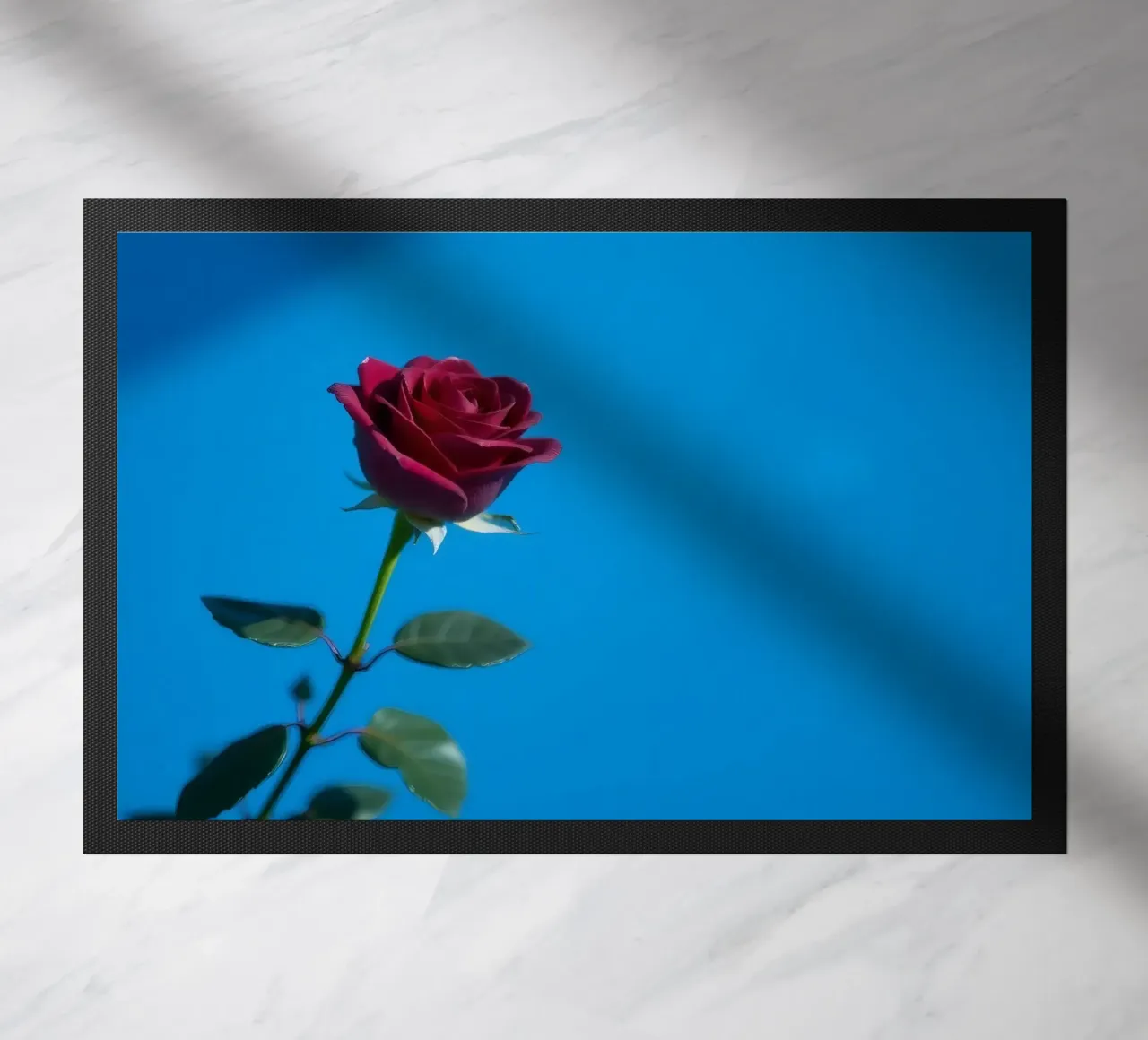 Une rose rouge vif s'épanouit sur un fond bleu vif. paillasson de DesignDoodle
