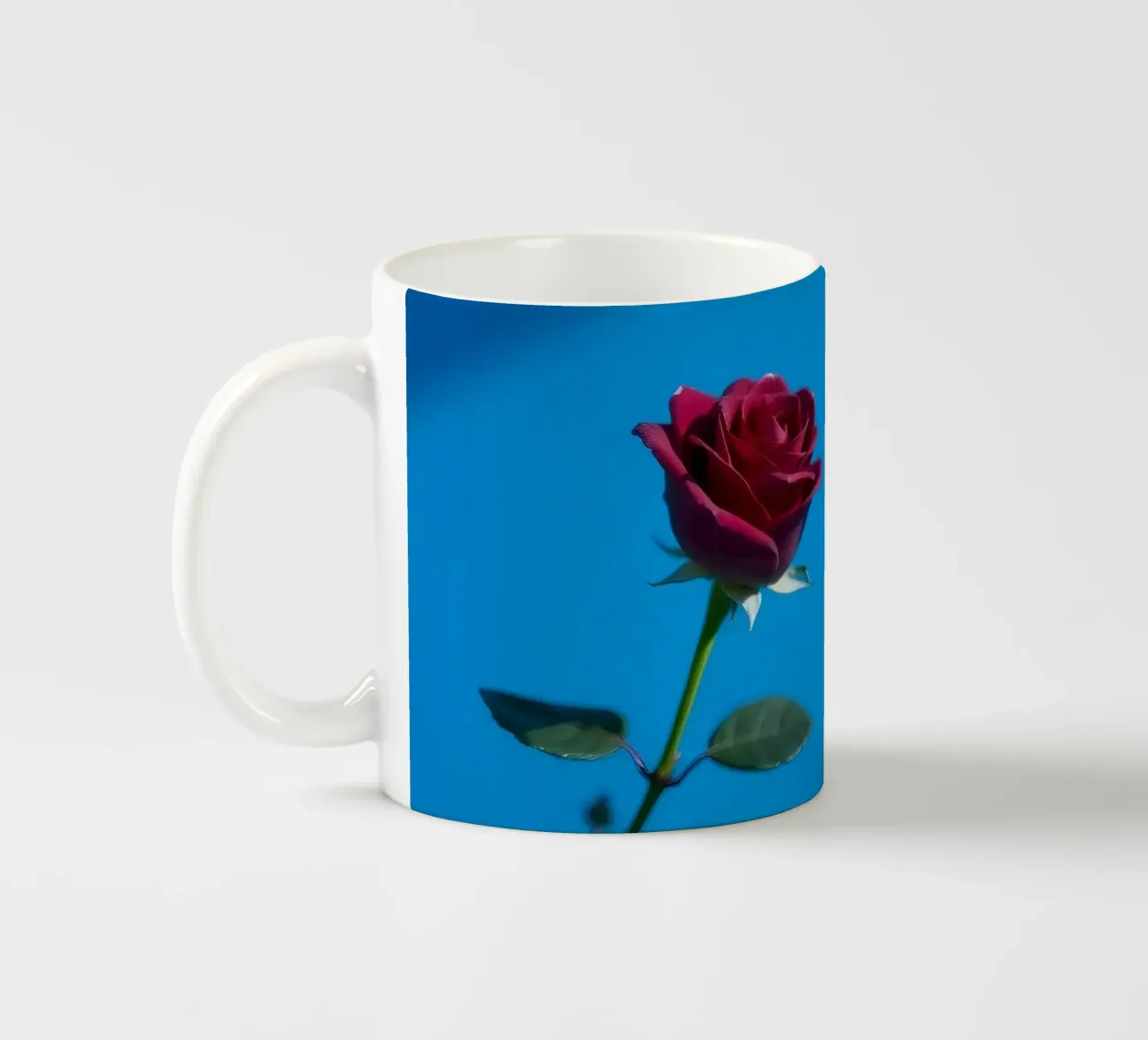 Une rose rouge vif s'épanouit sur un fond bleu vif. mug en céramique de DesignDoodle