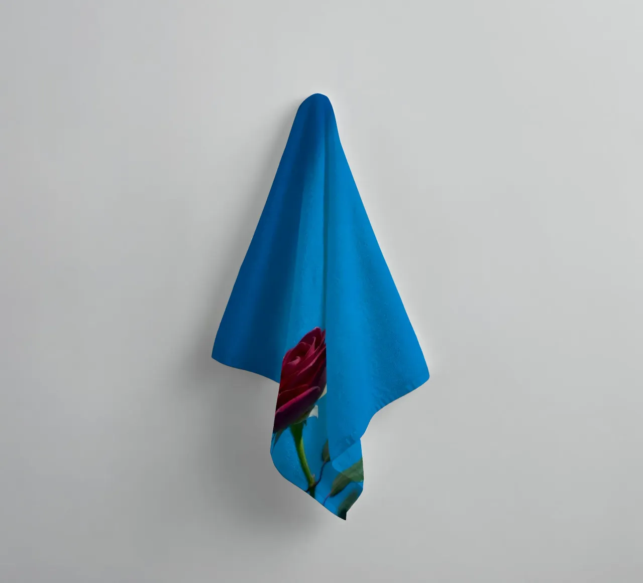 Une rose rouge vif s'épanouit sur un fond bleu vif. serviette de bain de DesignDoodle