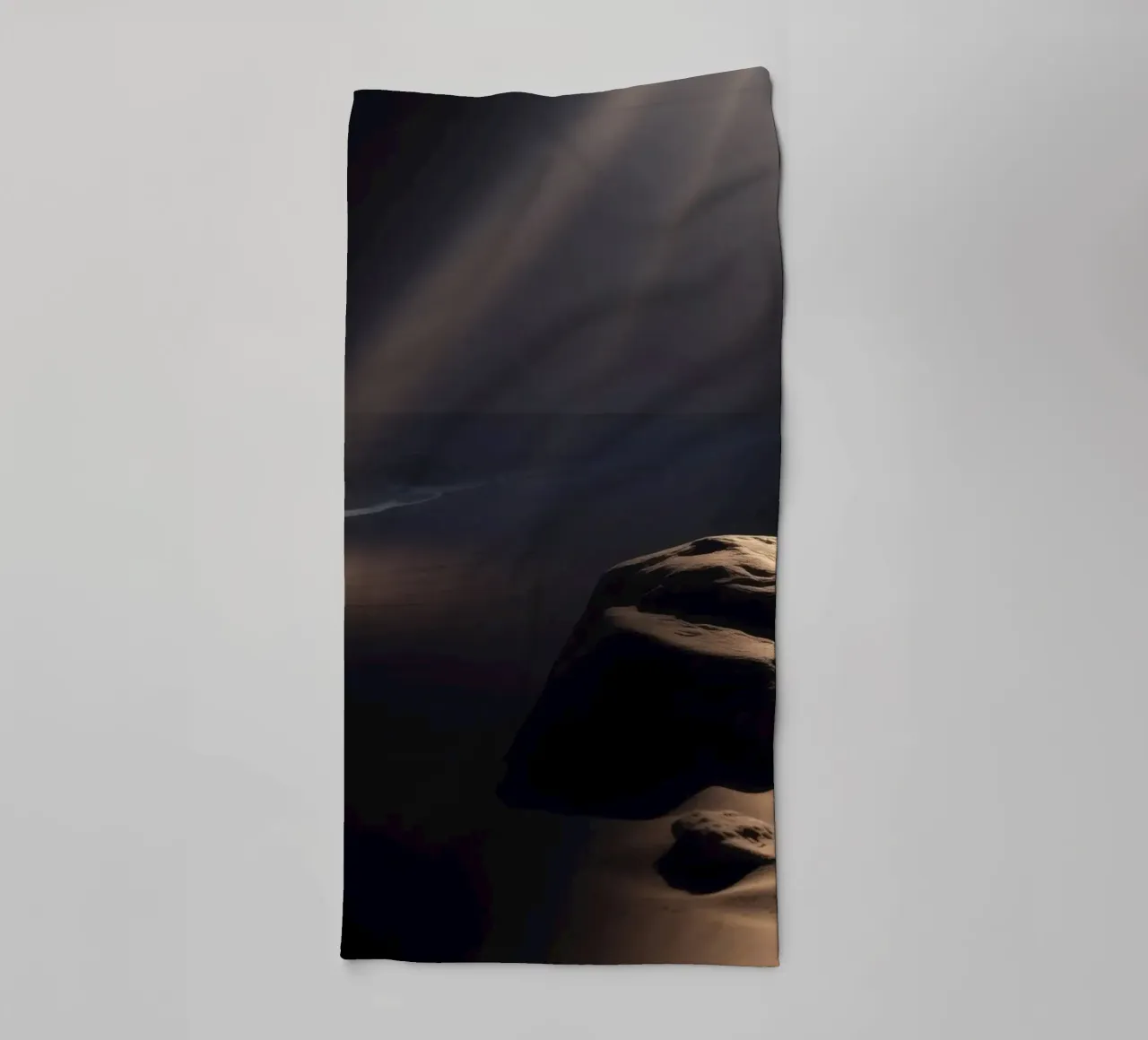 Fasci di luce illuminano una roccia solitaria su una spiaggia scura e sabbiosa asciugamano da bagno da DesignDoodle