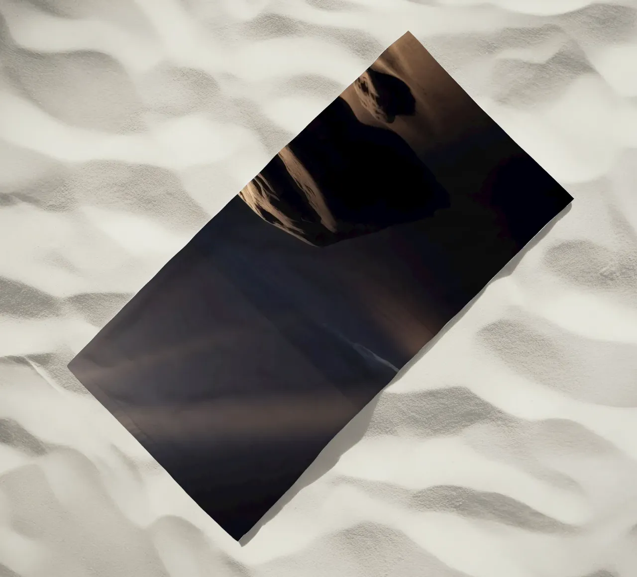 Fasci di luce illuminano una roccia solitaria su una spiaggia scura e sabbiosa telo mare da DesignDoodle