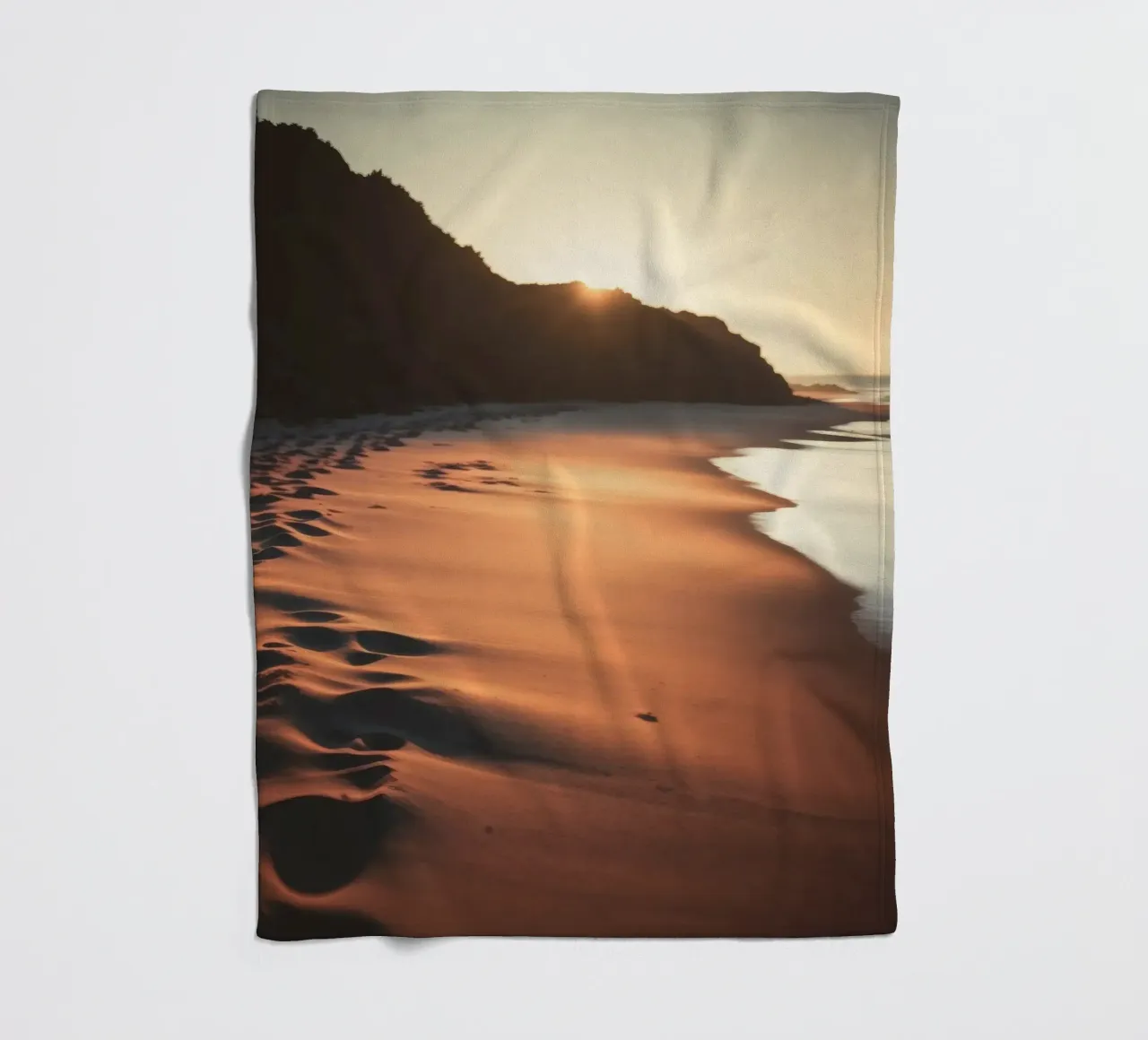 Sunset casts warm glow on sandy beach with gentle waves fleece blanket by DesignDoodle