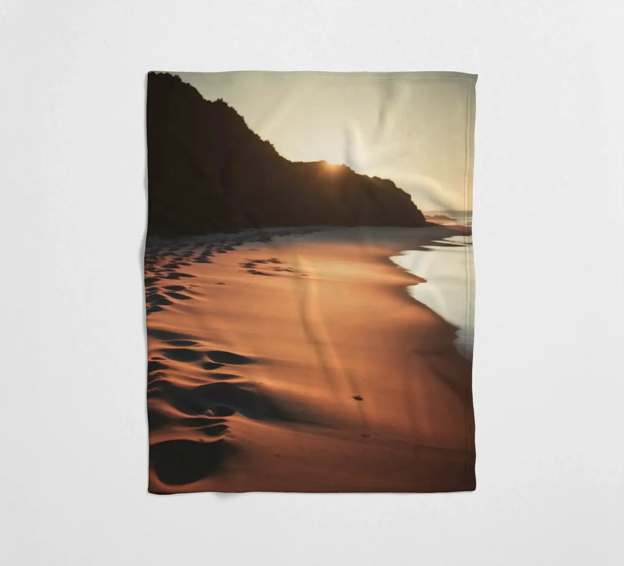 Sunset casts warm glow on sandy beach with gentle waves fleece blanket by DesignDoodle