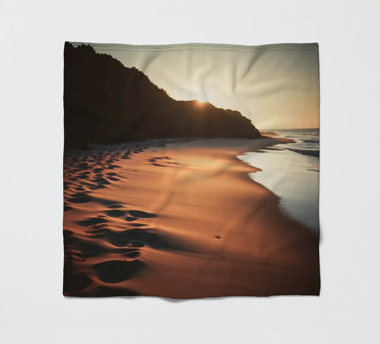 Sunset casts warm glow on sandy beach with gentle waves fleece blanket by DesignDoodle