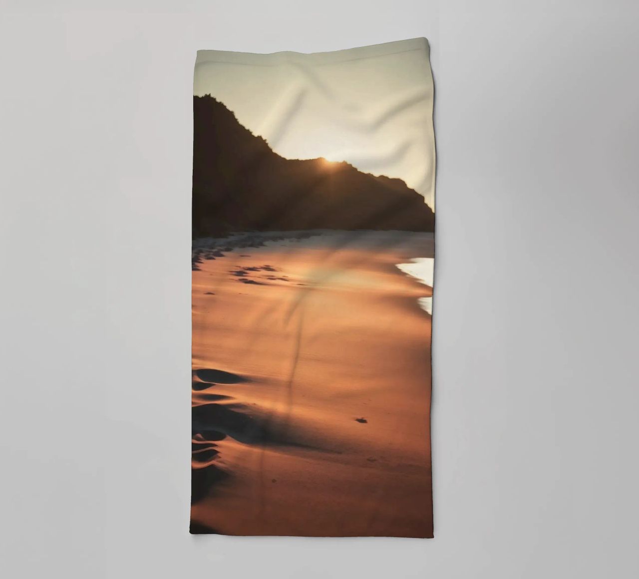 Zonsondergang werpt warme gloed op zandstrand met zachte golven badhanddoek van DesignDoodle