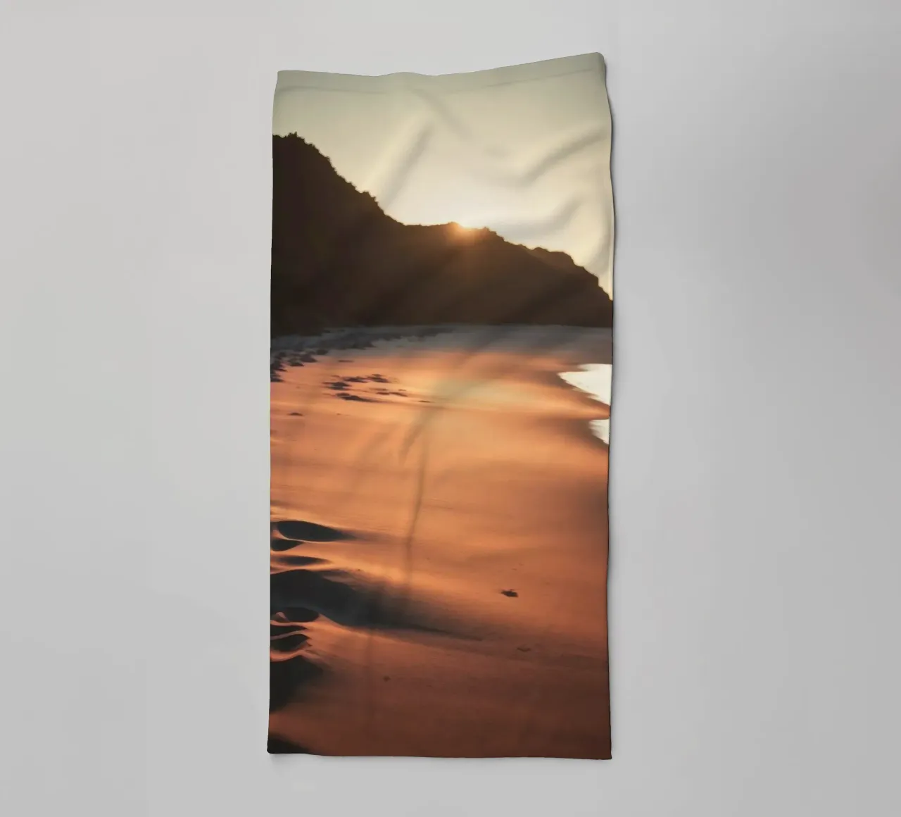 Il tramonto proietta una calda luce sulla spiaggia sabbiosa con le sue dolci onde asciugamano da bagno da DesignDoodle