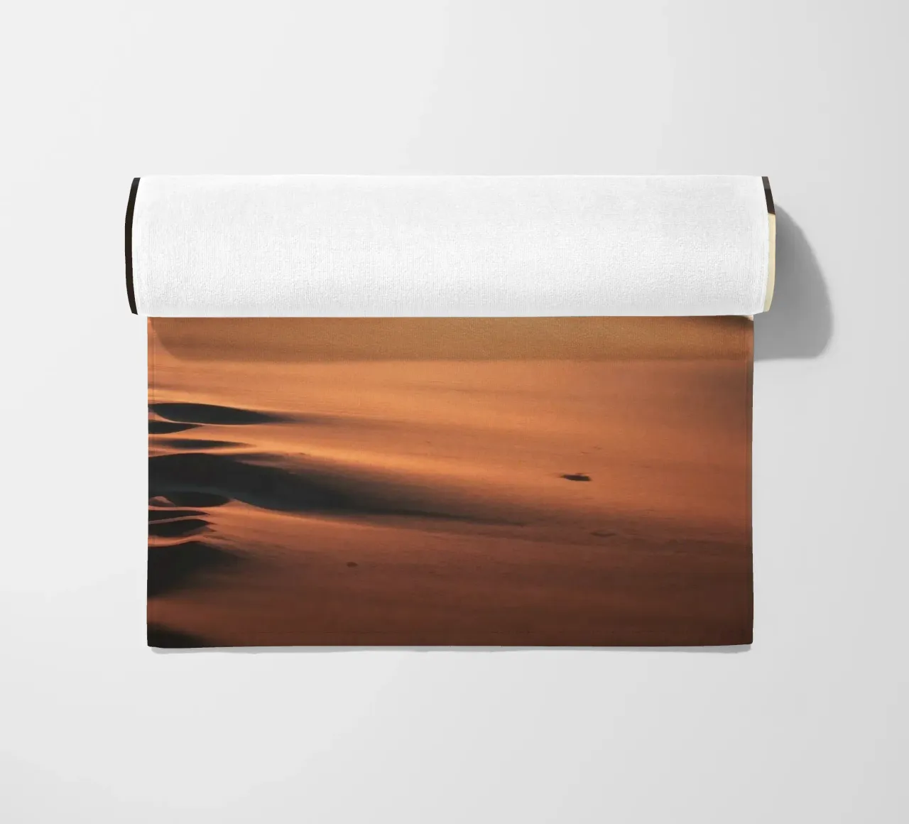 Sunset casts warm glow on sandy beach with gentle waves beach towel by DesignDoodle