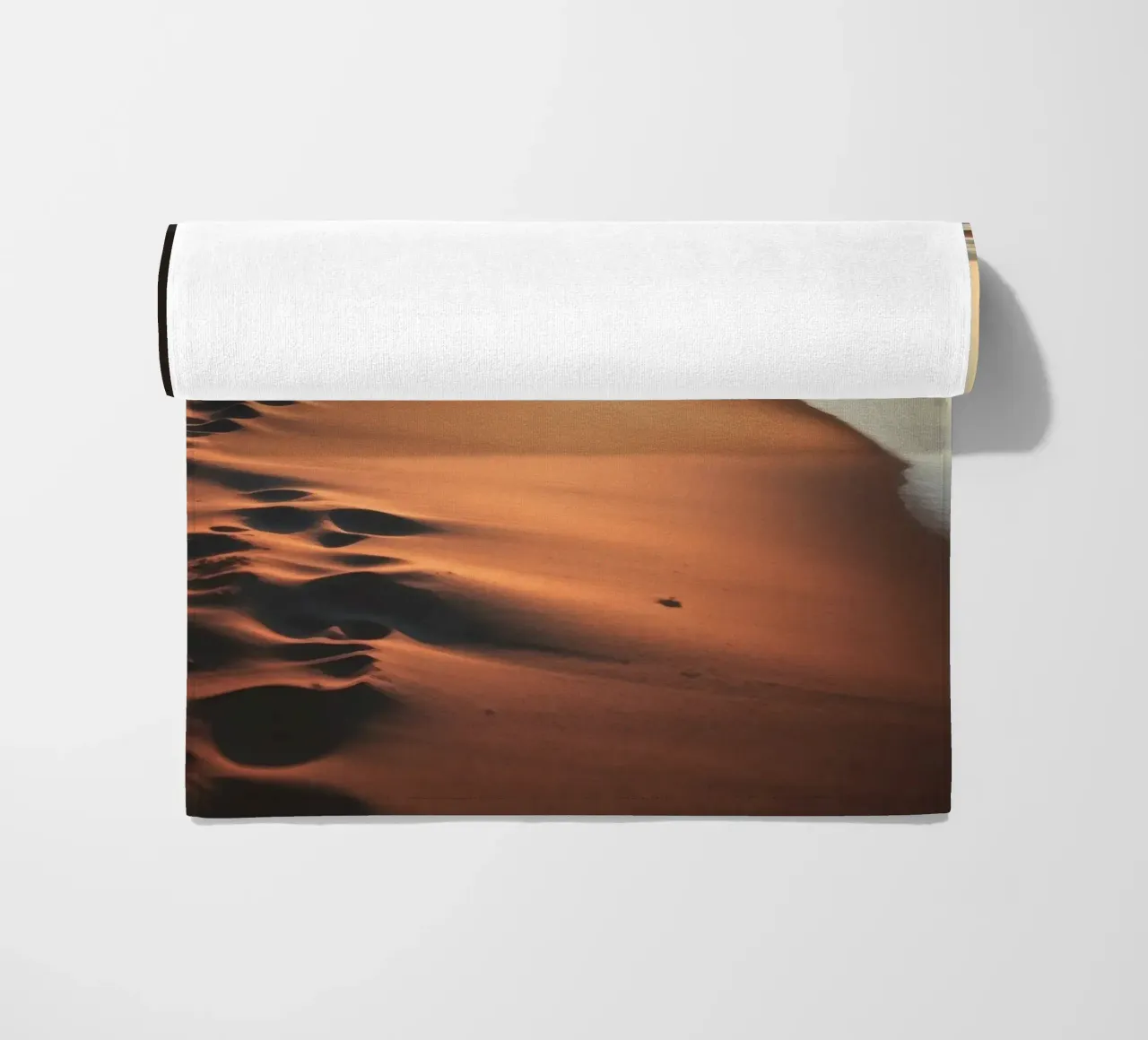 Sunset casts warm glow on sandy beach with gentle waves beach towel by DesignDoodle