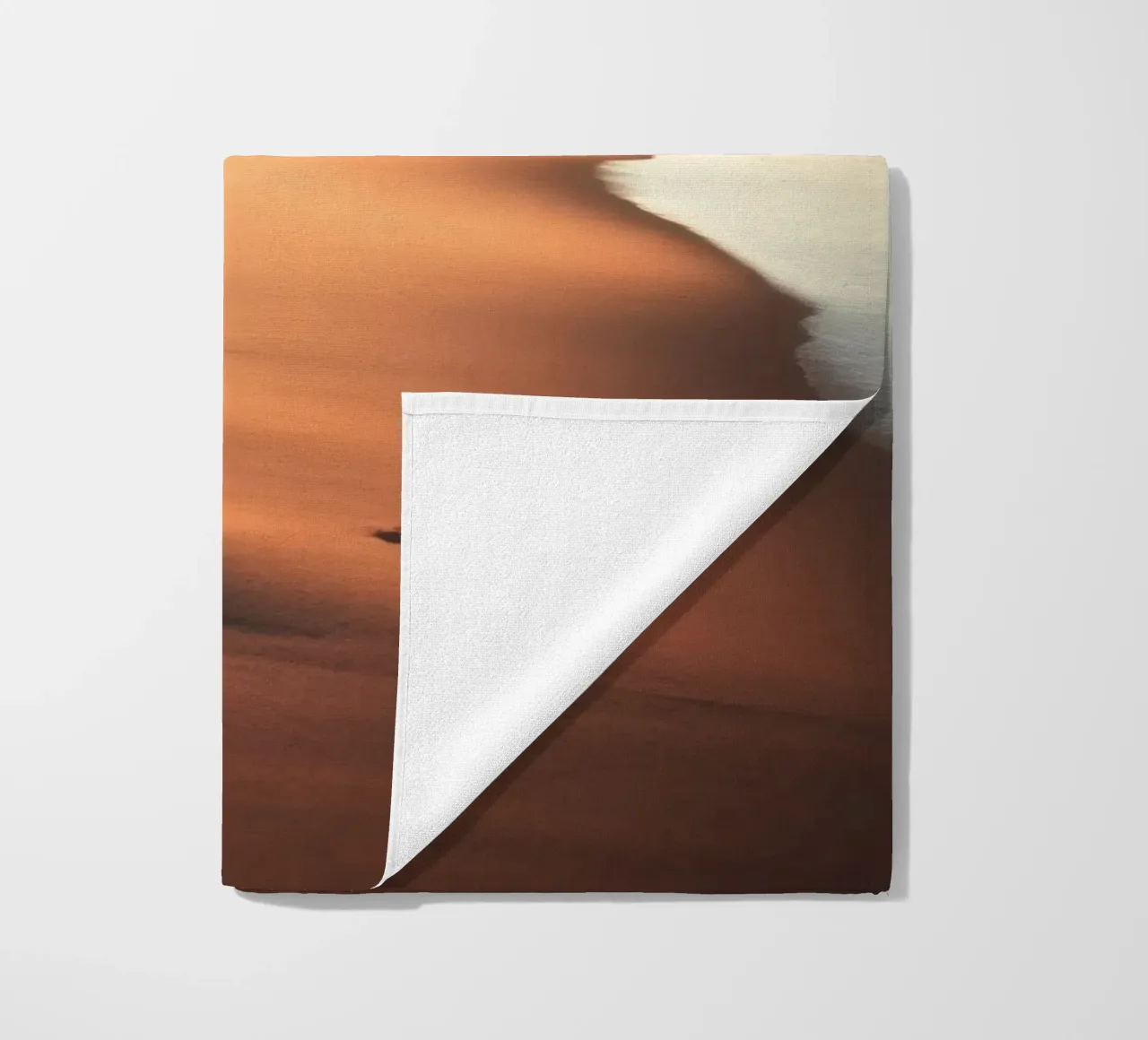 Sunset casts warm glow on sandy beach with gentle waves beach towel by DesignDoodle