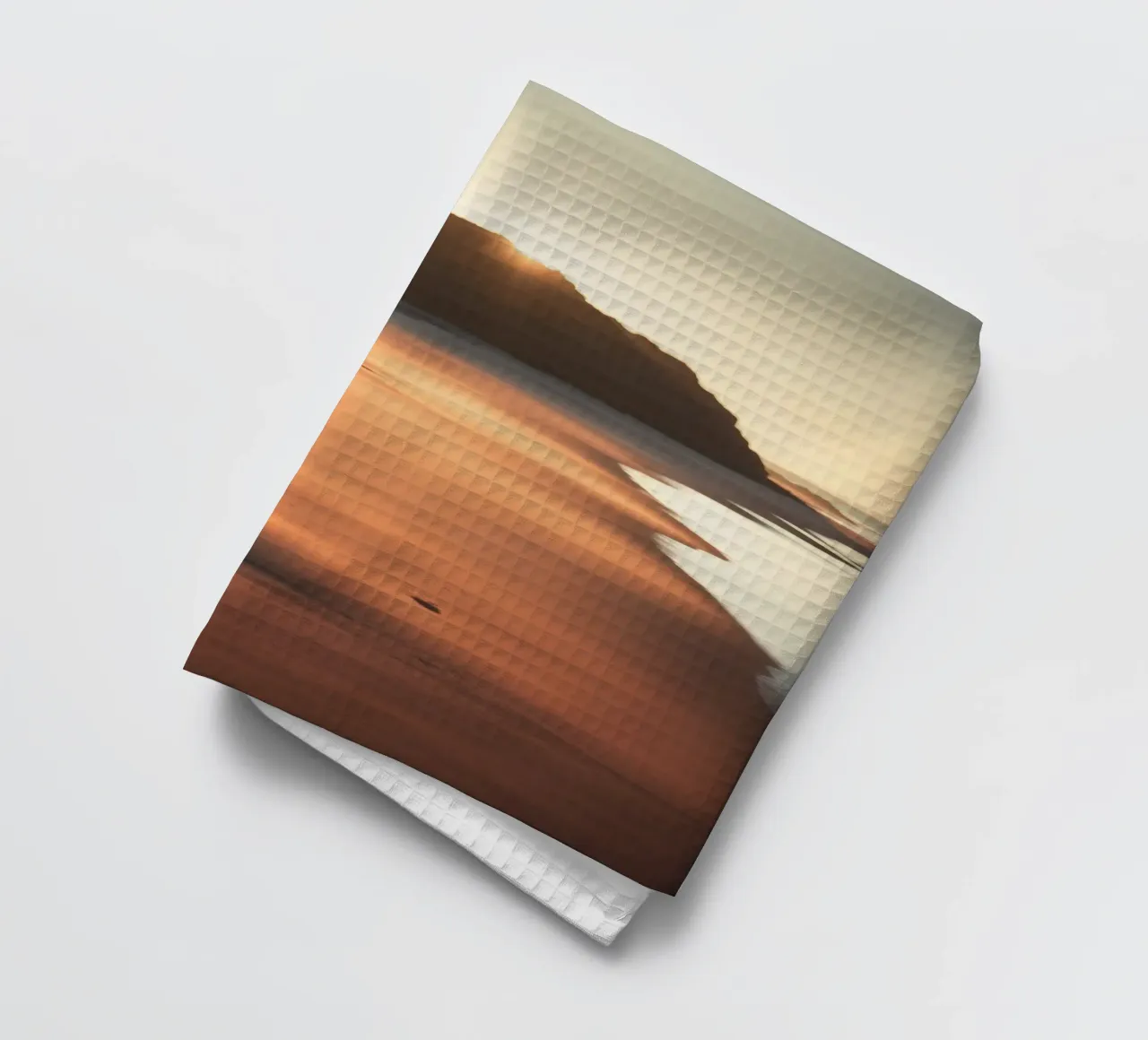 Le coucher de soleil jette une lumière chaude sur une plage de sable avec de douces vagues. torchon de DesignDoodle