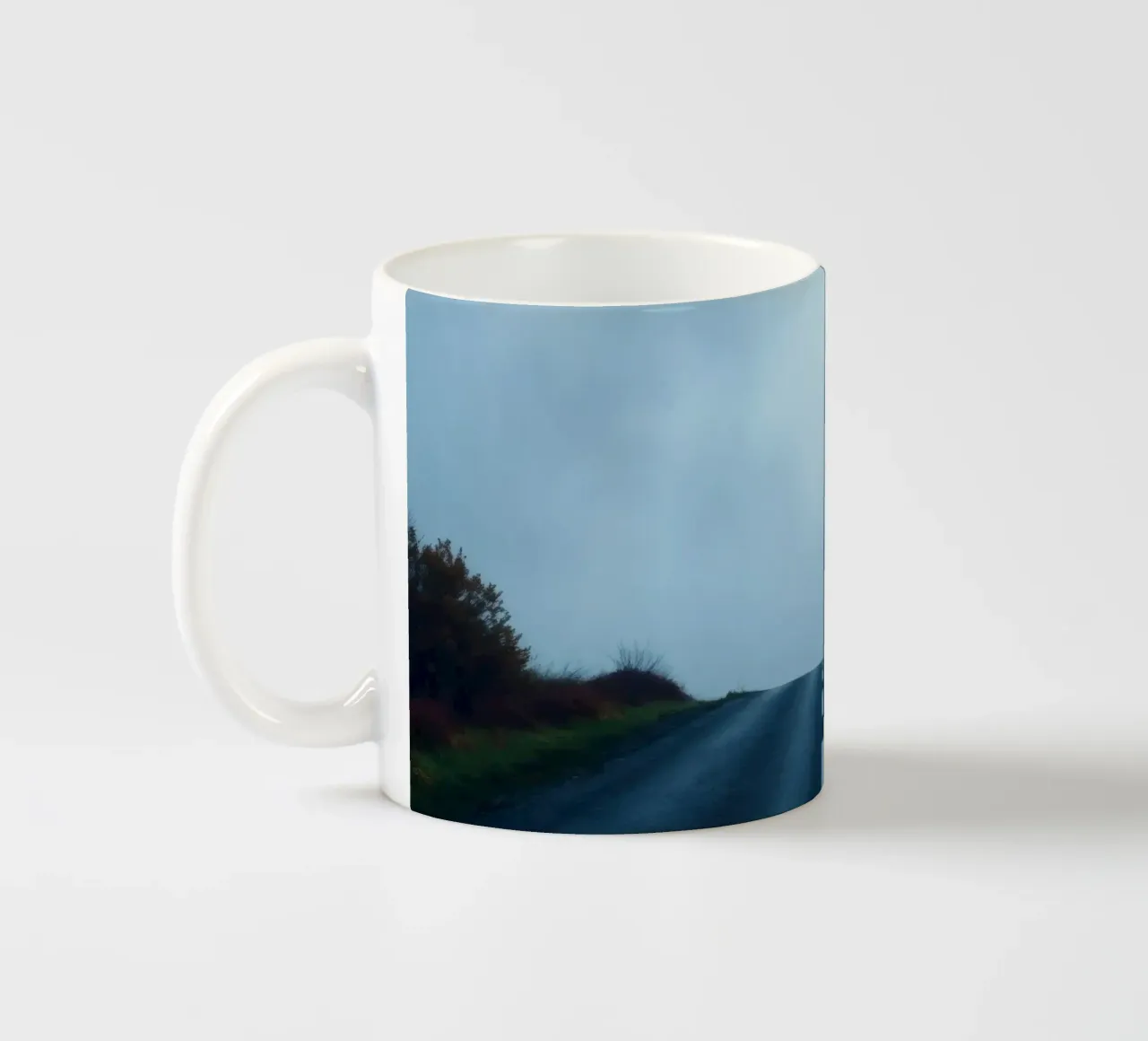 la strada si inoltra nella nebbia, con il verde su entrambi i lati tazza in ceramica da DesignDoodle