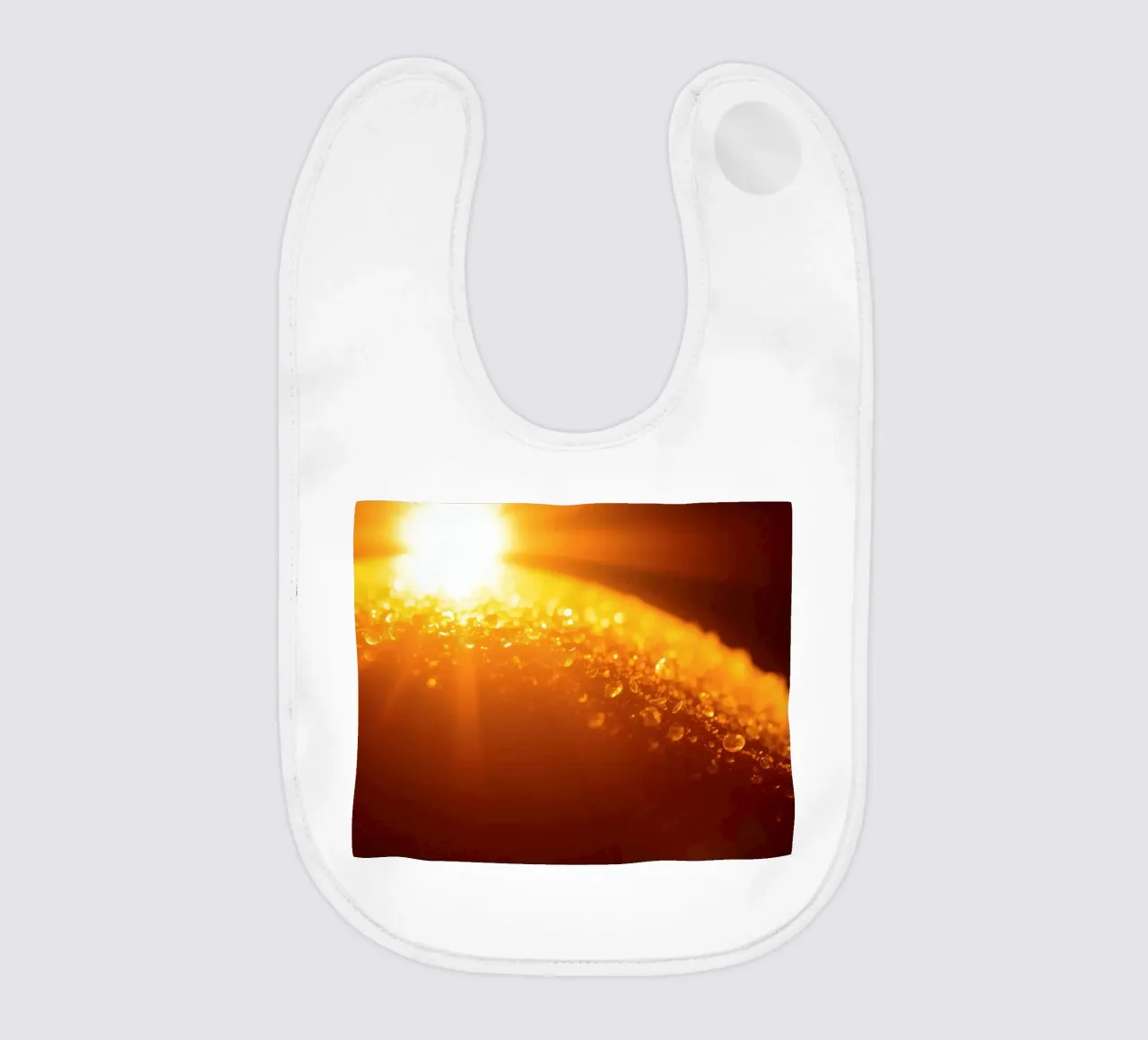 Sunlight glistens on a dewy surface at dawn, creating a warm baby bib by DesignDoodle